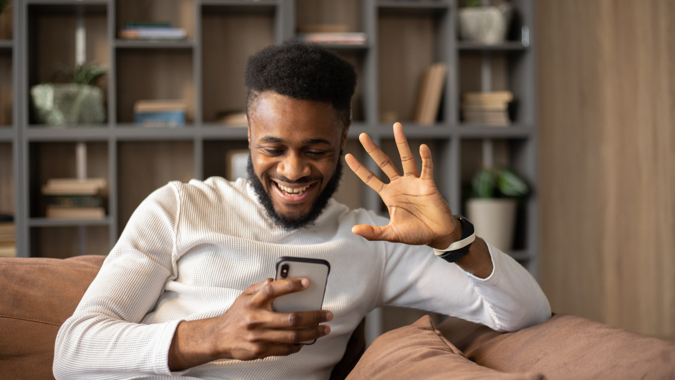 Smiling man waving while looking at smartphone