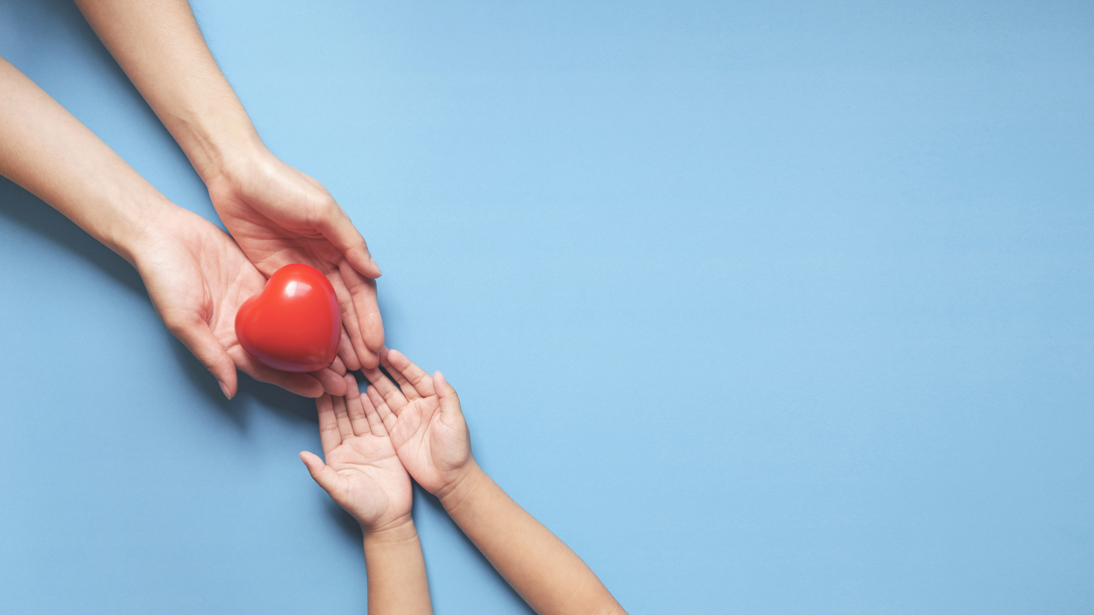 Adult hands giving red heart to child hands on blue background
