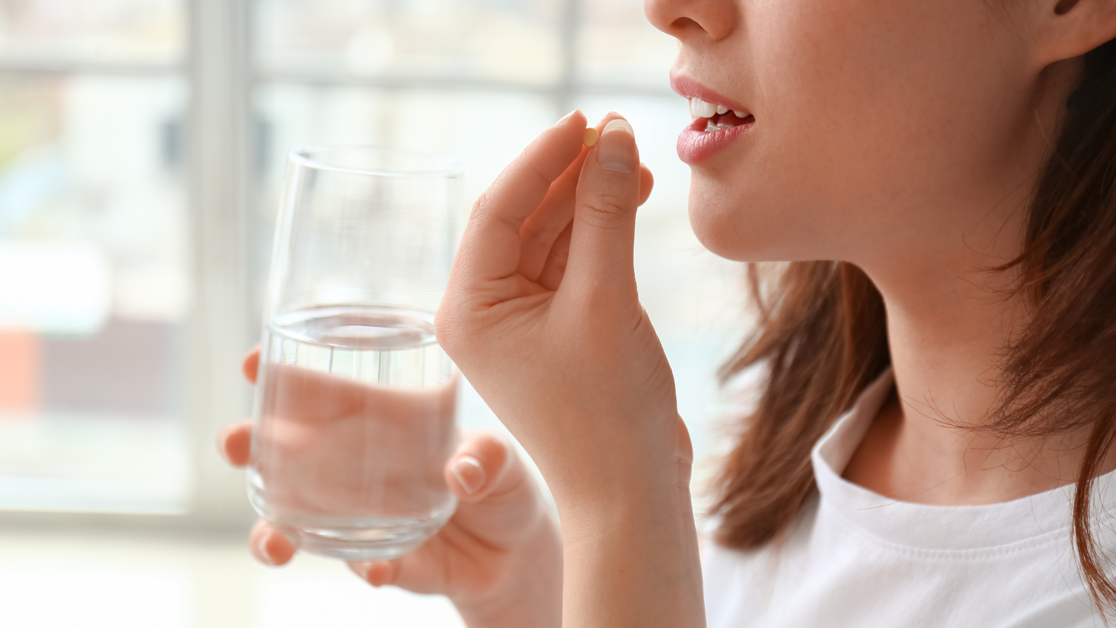 Person holding a pill and a glass of water near their mouth