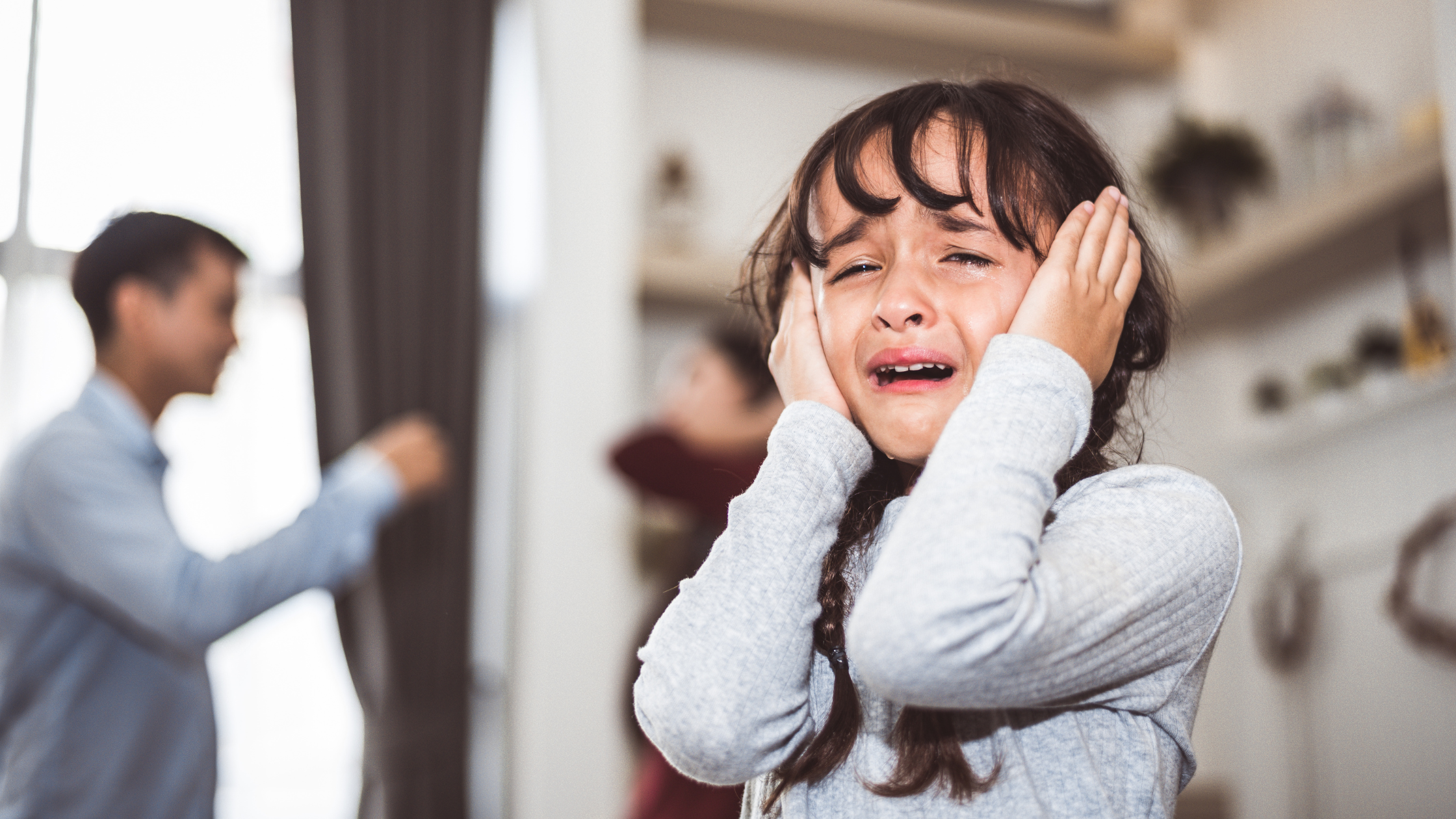 Crying girl covering ears with blurred adults arguing in background