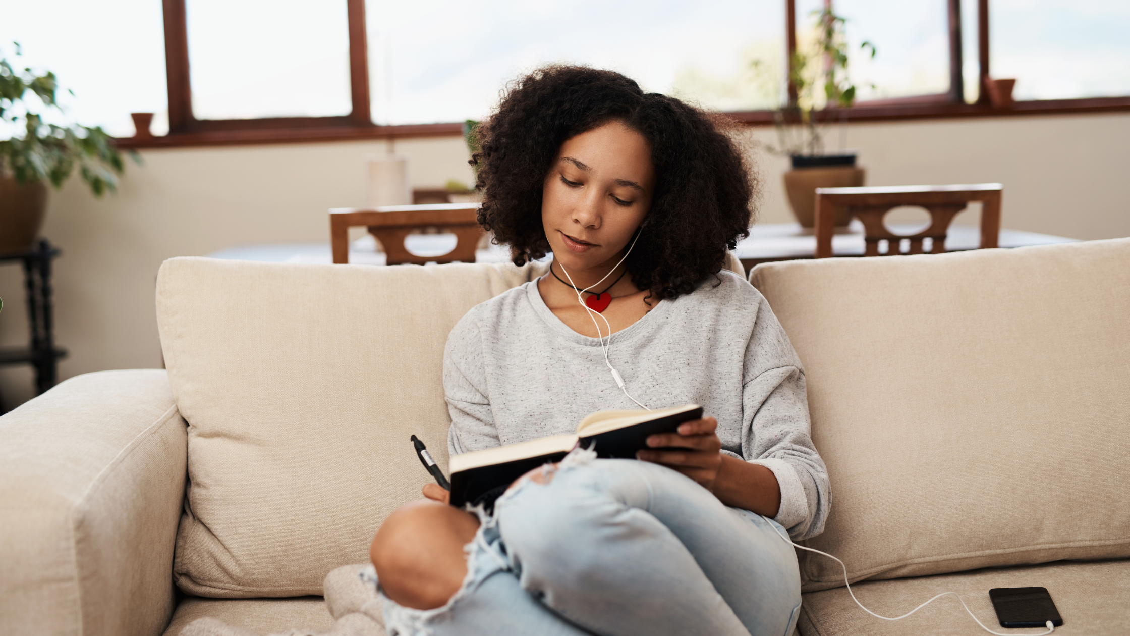Person sitting on couch writing in journal with earbuds in