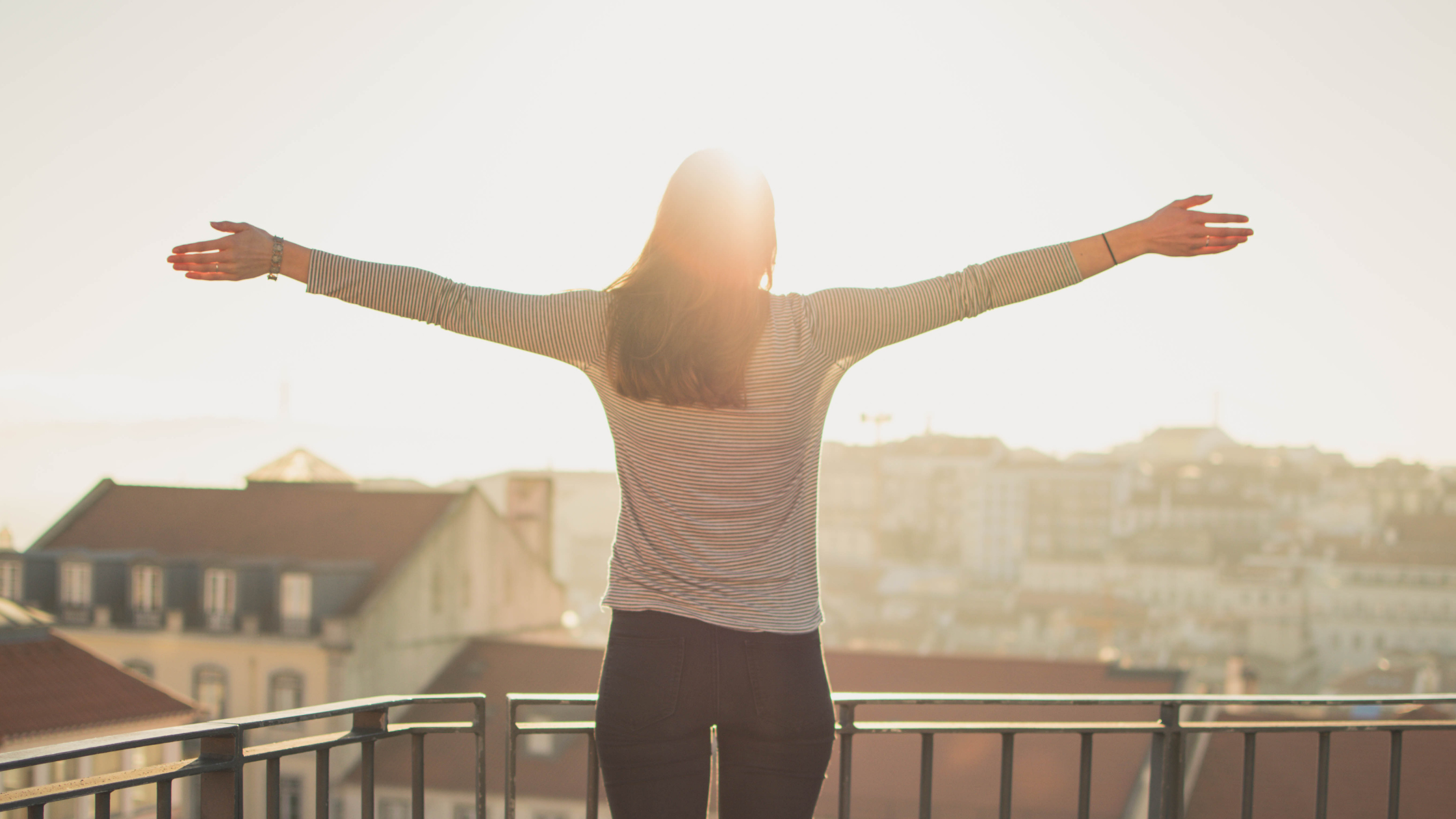 Person standing on balcony with arms outstretched towards sunlight