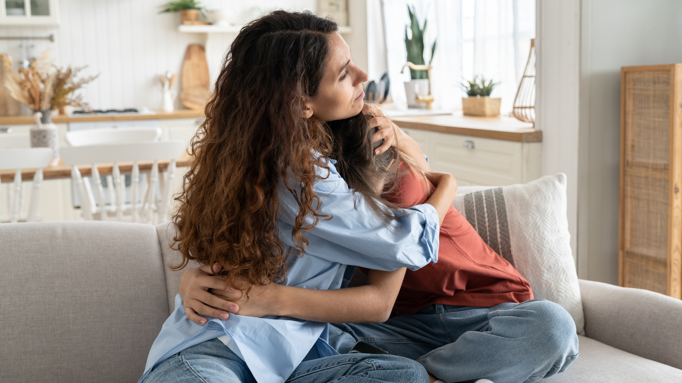 Two people sitting on couch comforting each other with embrace