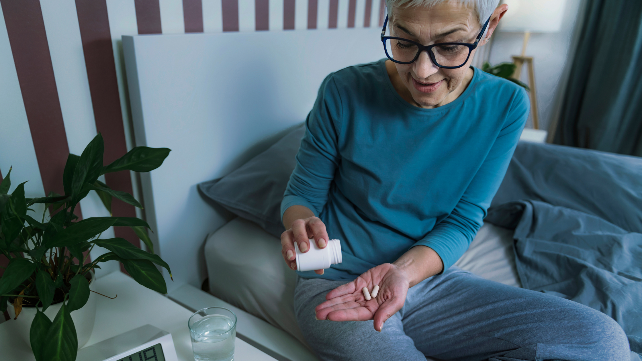 Person taking capsules beside a bed with a glass of water