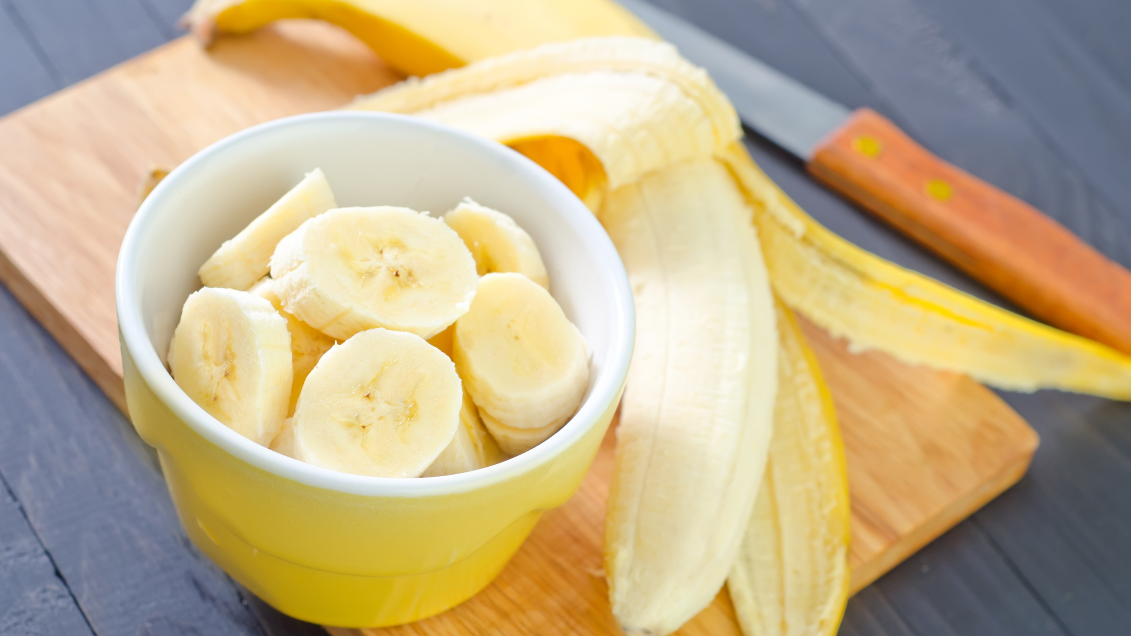 Sliced bananas in a yellow bowl next to a peeled banana