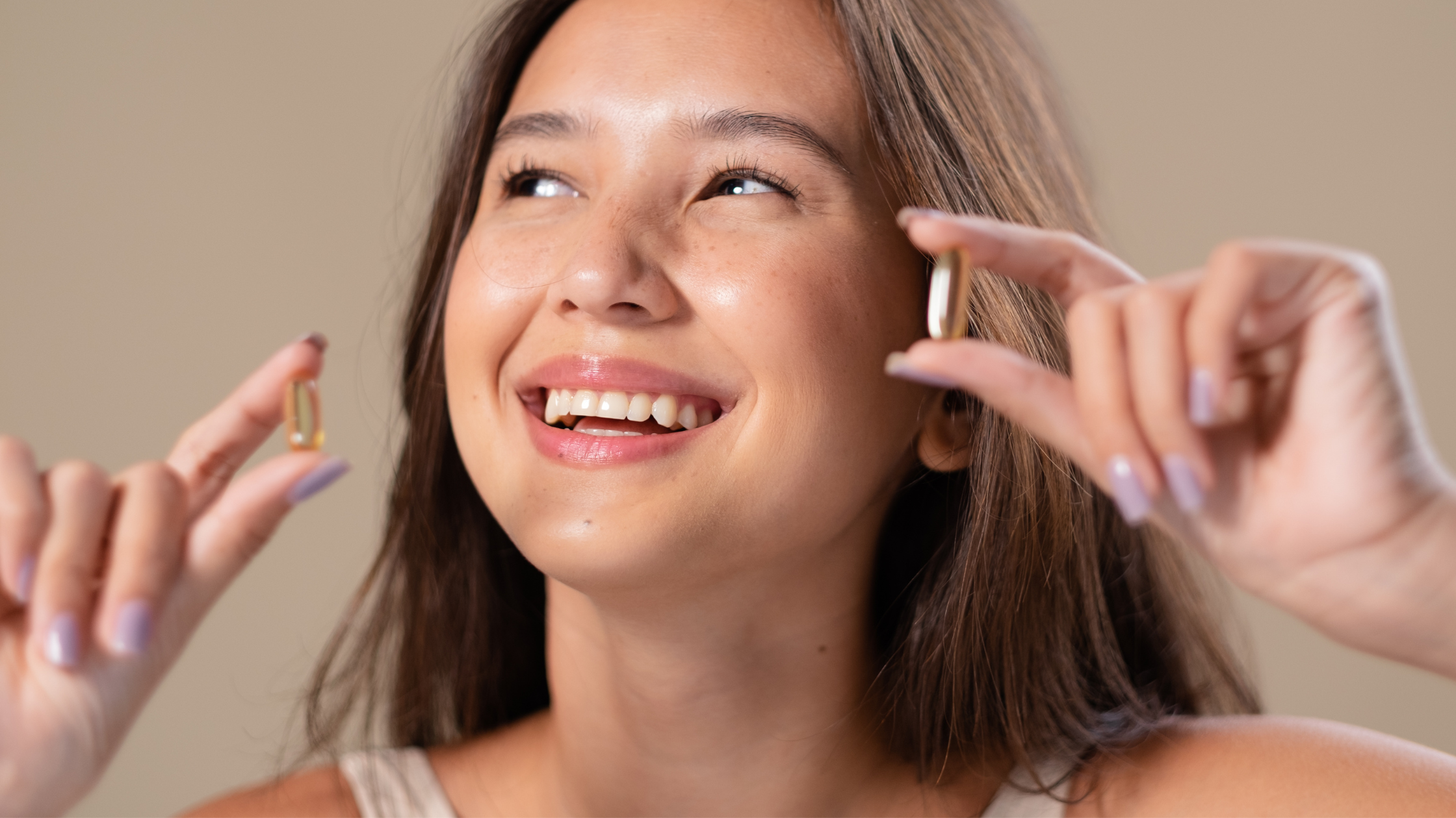 Smiling woman holding two translucent supplements near her face