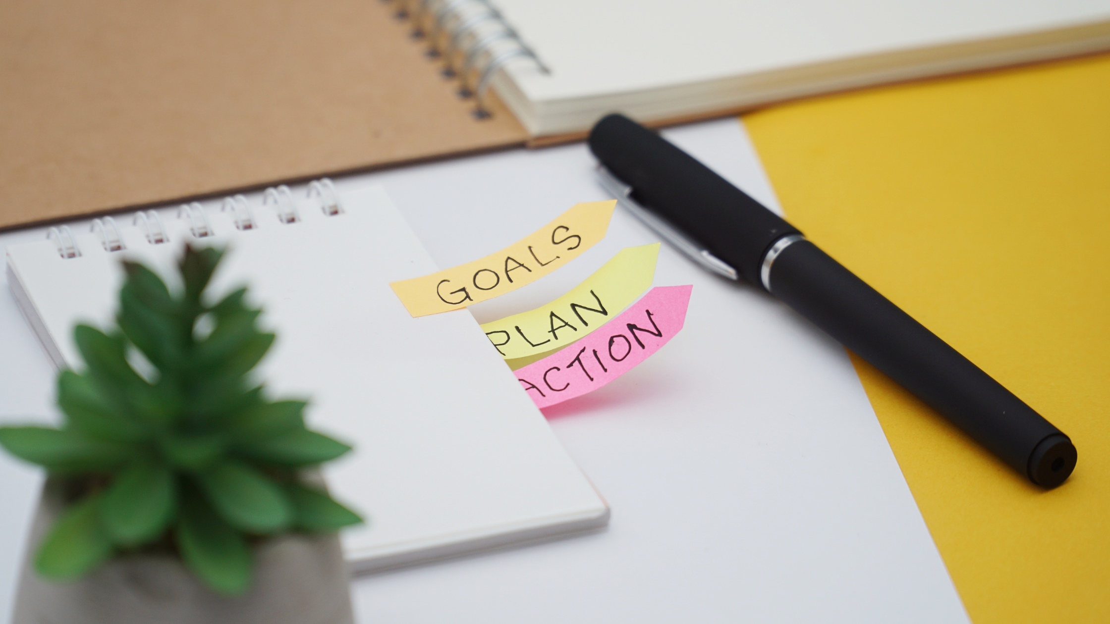 Notepad with sticky notes labeled goals, plan, action and black pen