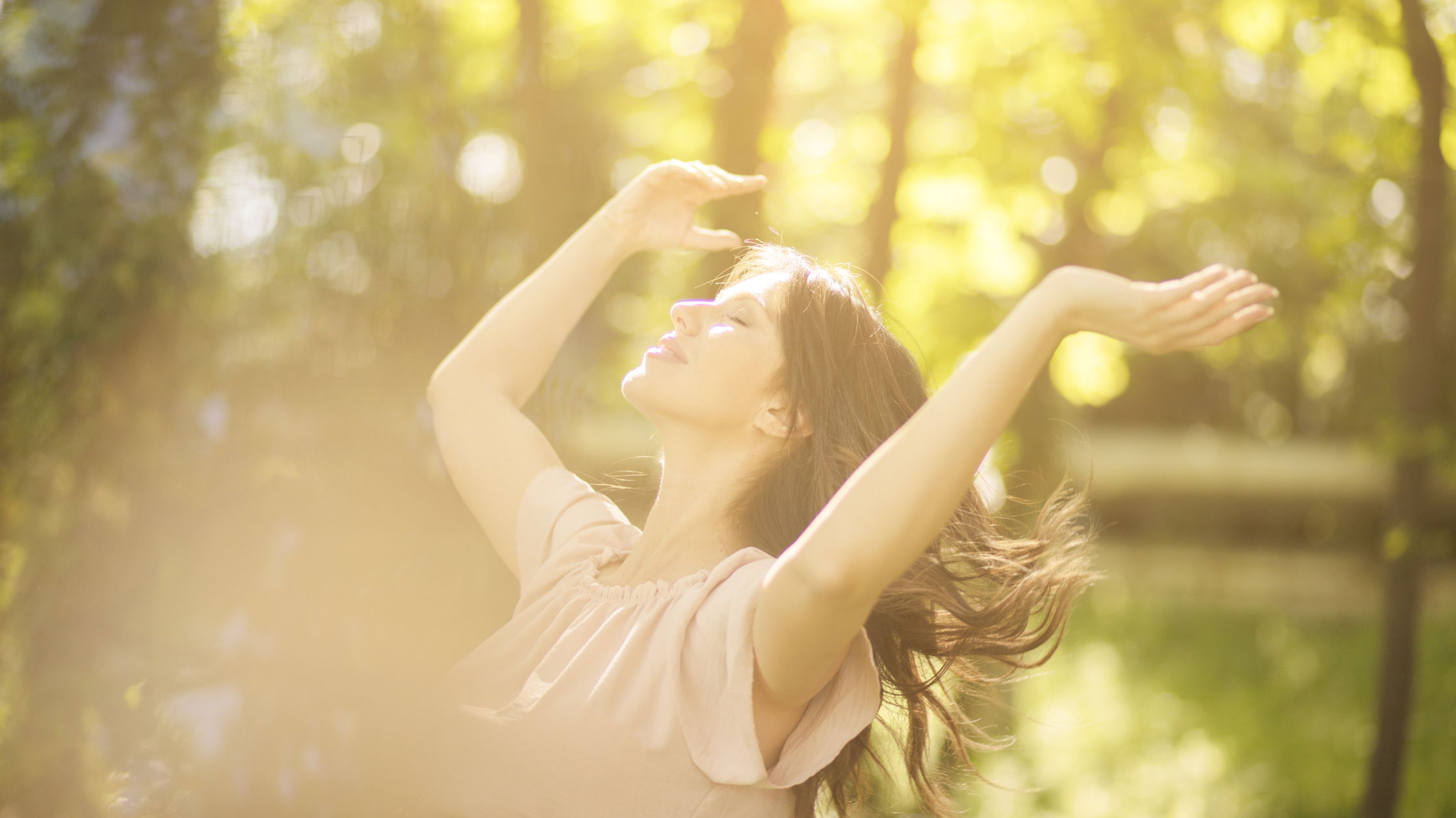 Woman with arms raised enjoying sunlight outdoors