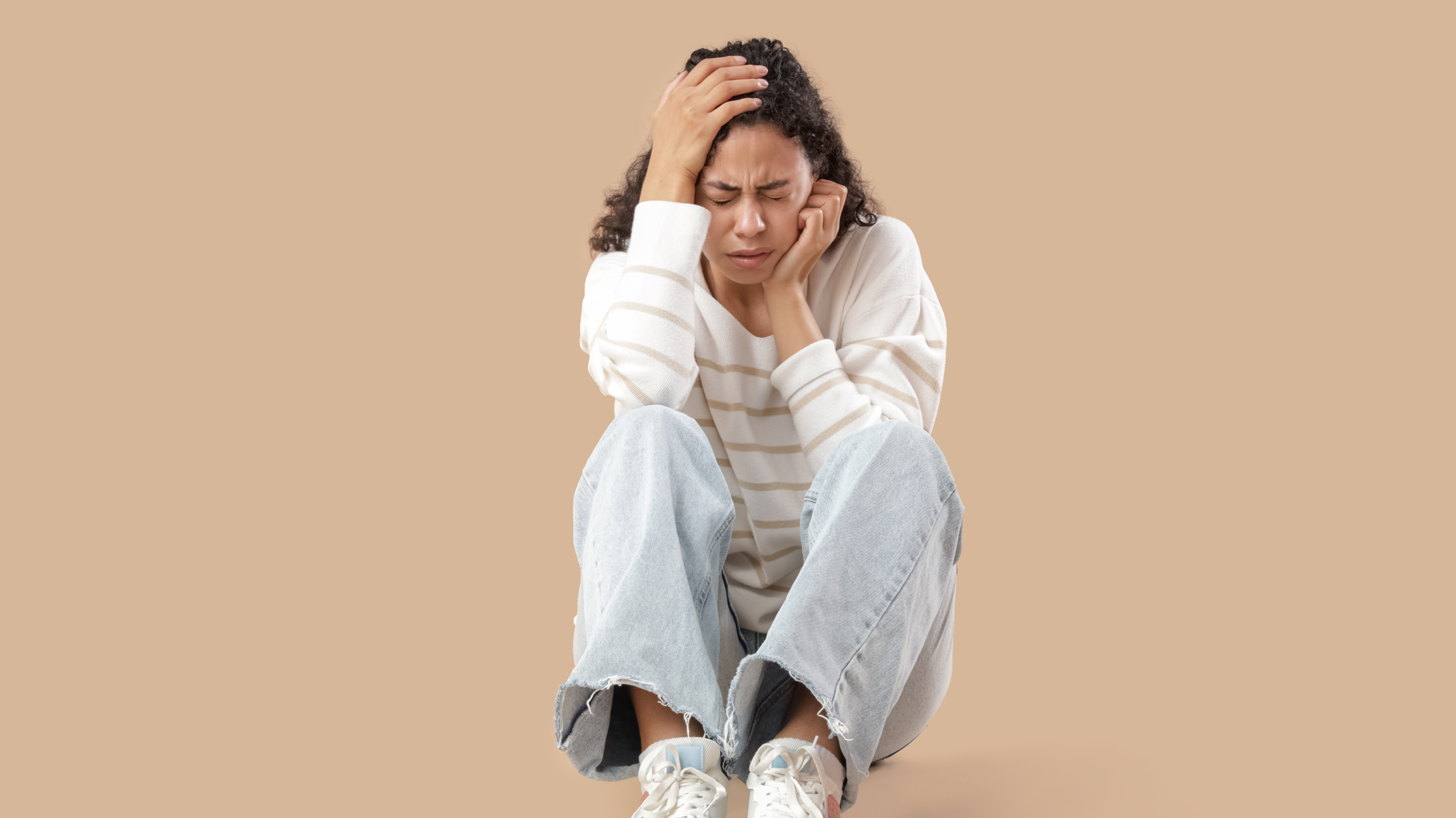 Woman sitting on floor with eyes closed, holding head in distress