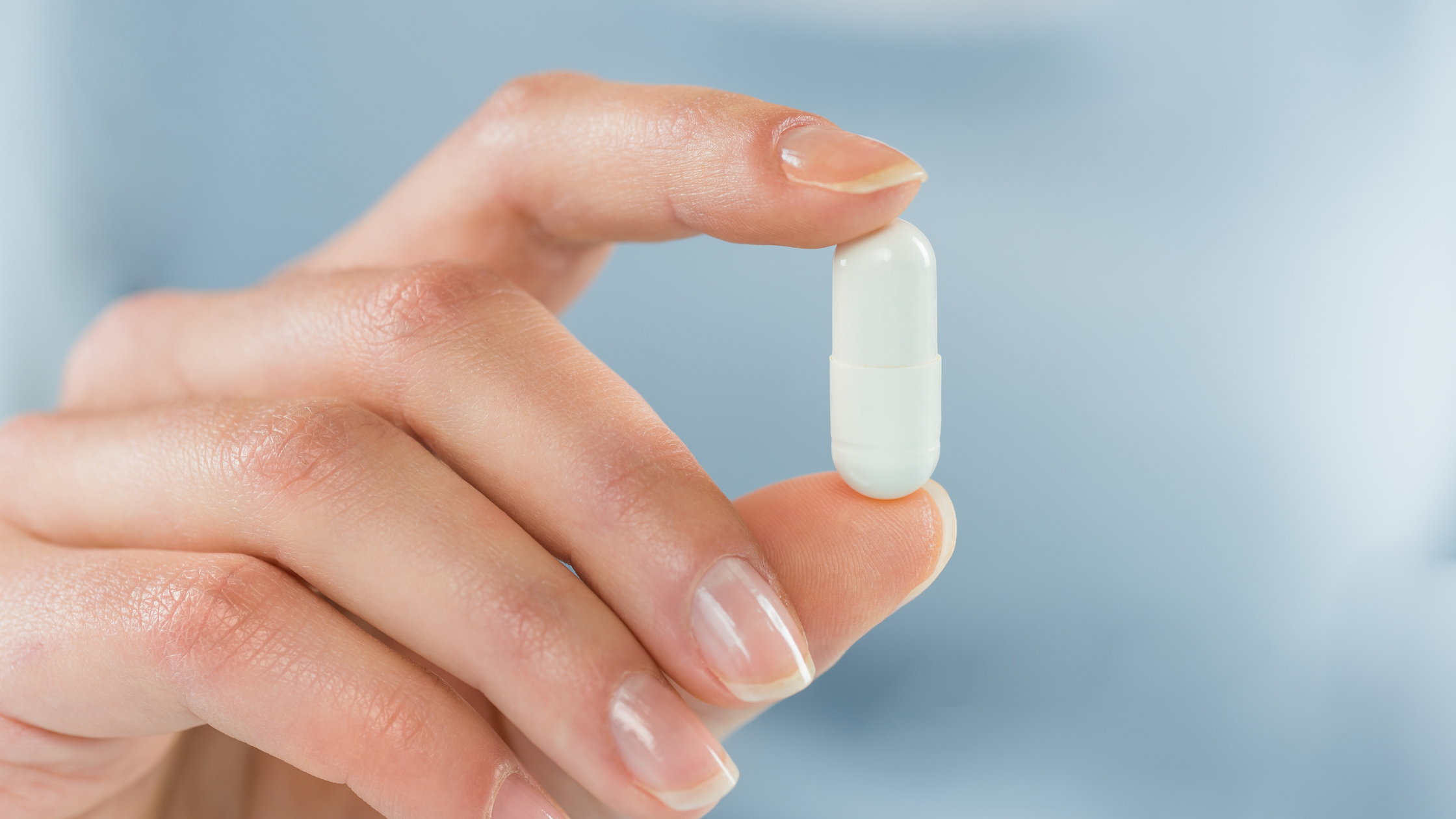 Hand holding a single white capsule pill