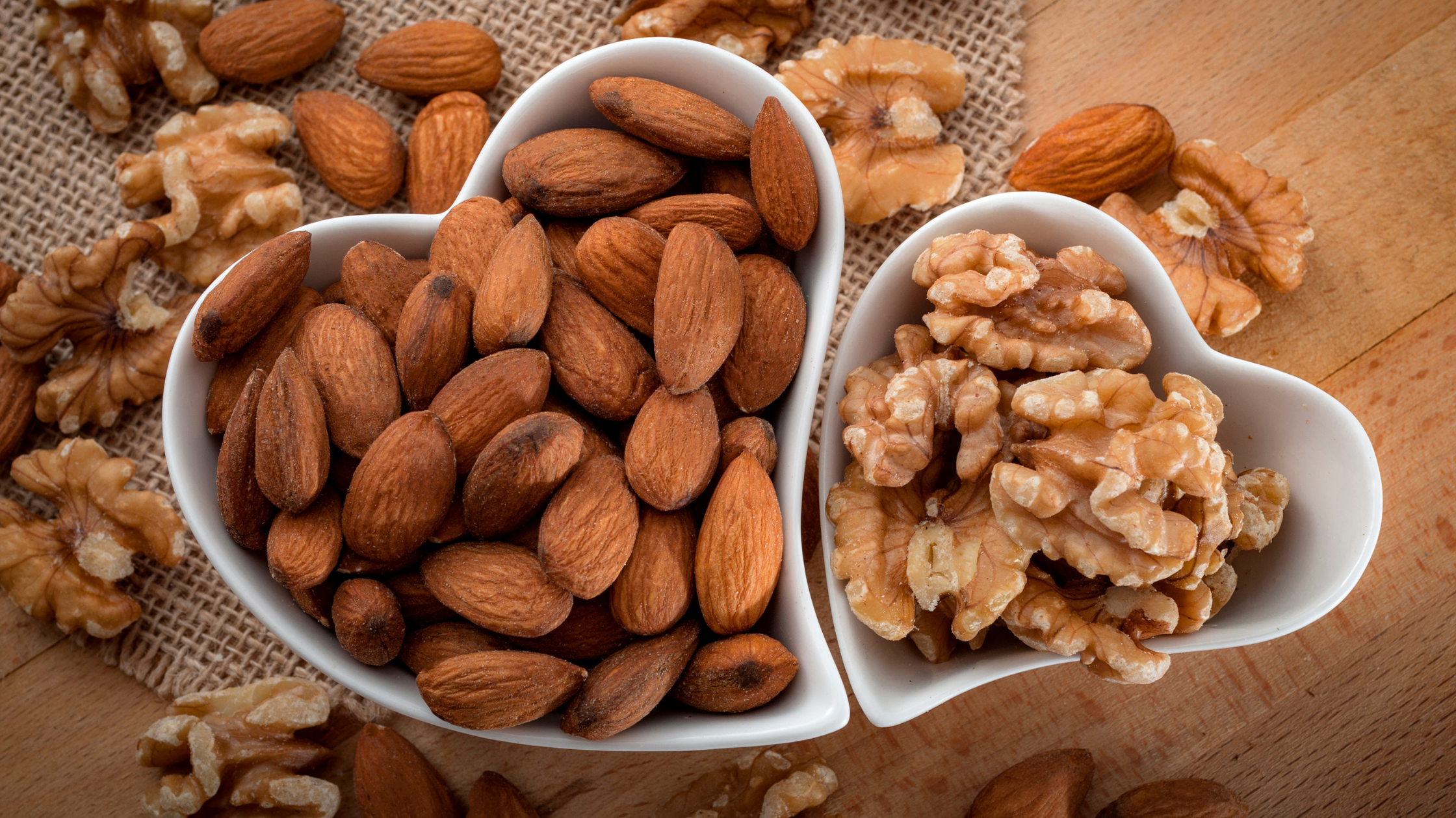 Almonds and walnuts in heart-shaped bowls on a wooden surface