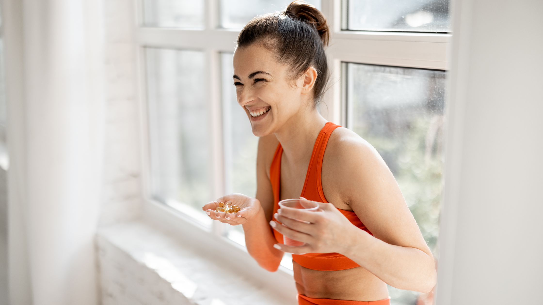 Smiling woman in exercise outfit holding capsules and a glass of water