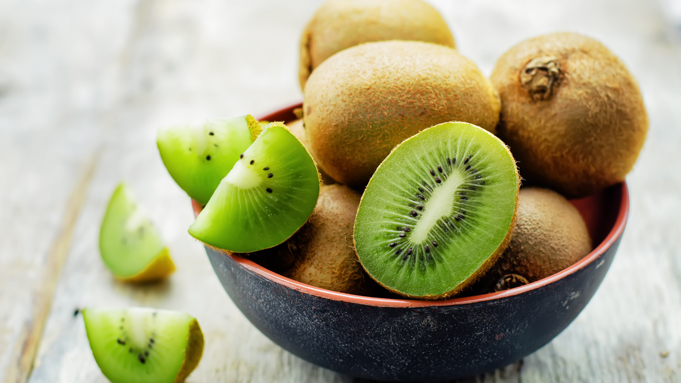 Bowl of whole and sliced kiwi fruits on a wooden surface