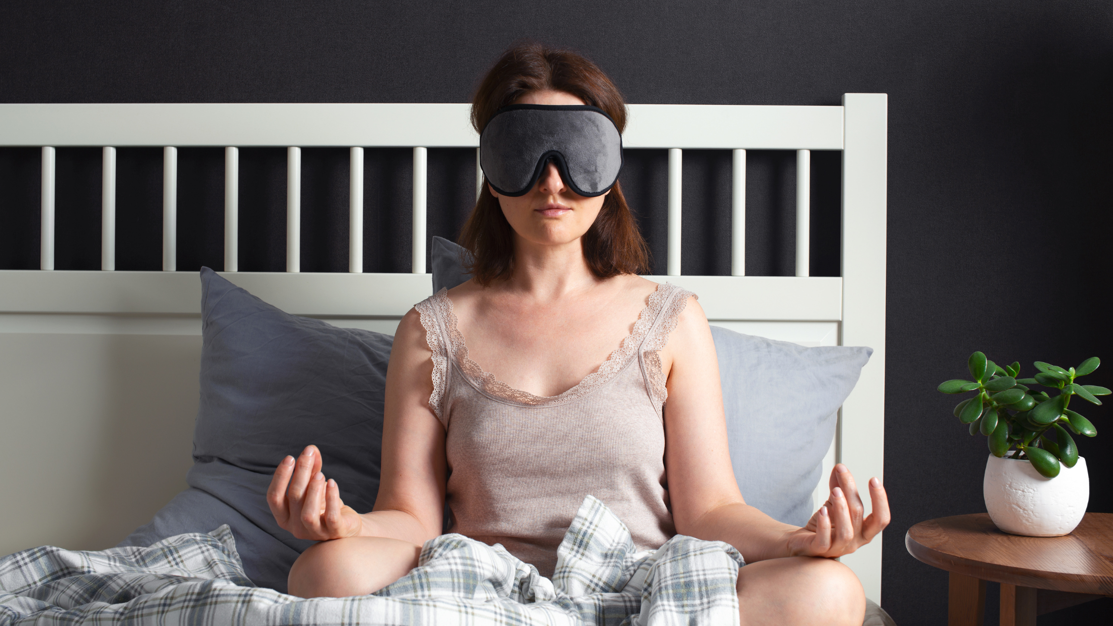 Woman wearing sleep mask meditating on bed