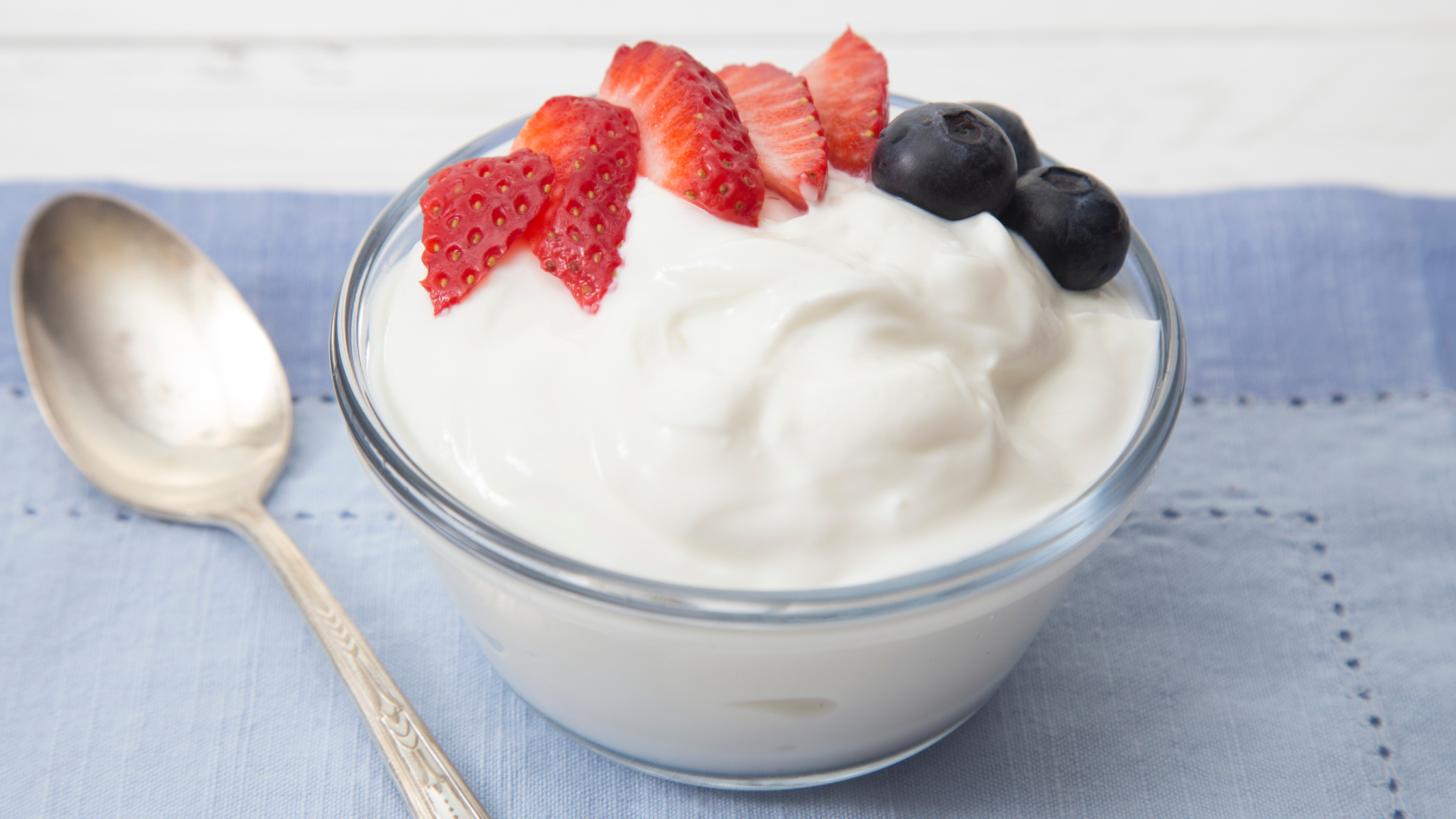 Bowl of yogurt topped with sliced strawberries and blueberries