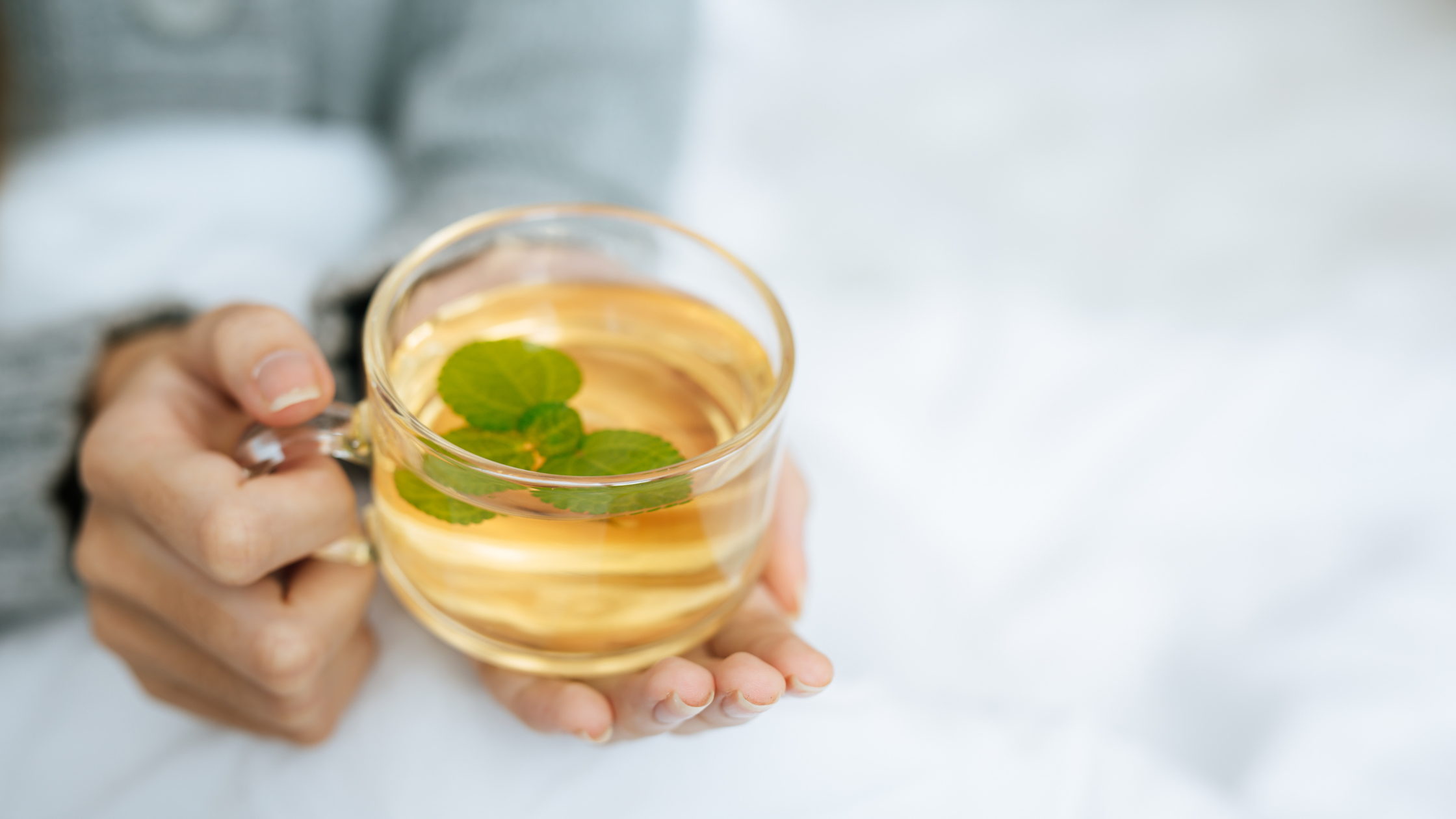 Hand holding a glass cup of herbal tea with mint leaves