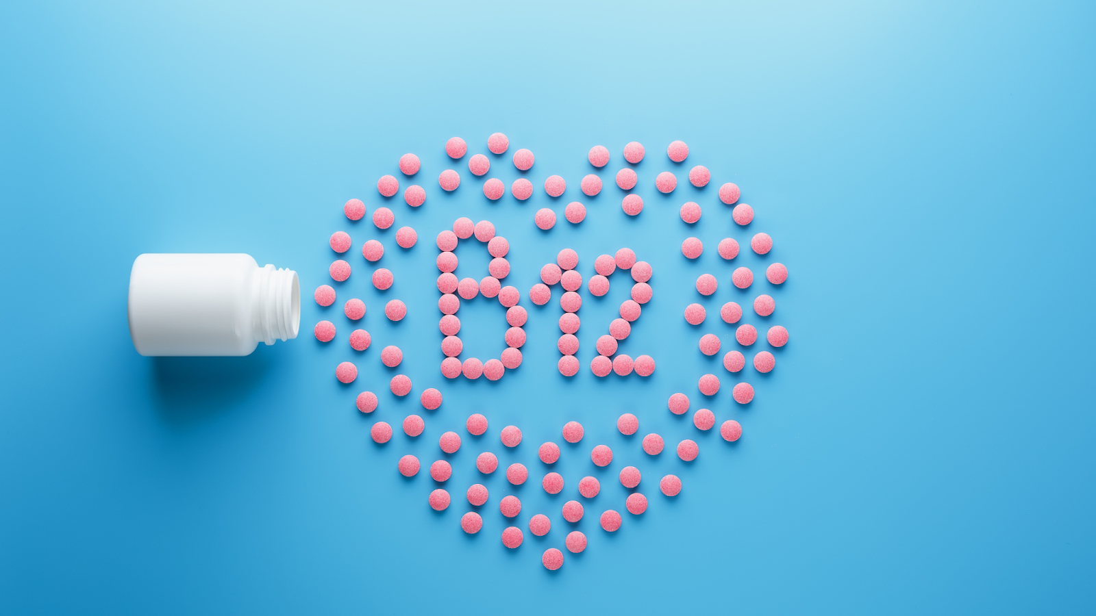 Pink pills arranged in a heart shape with B12 in the center next to a white bottle