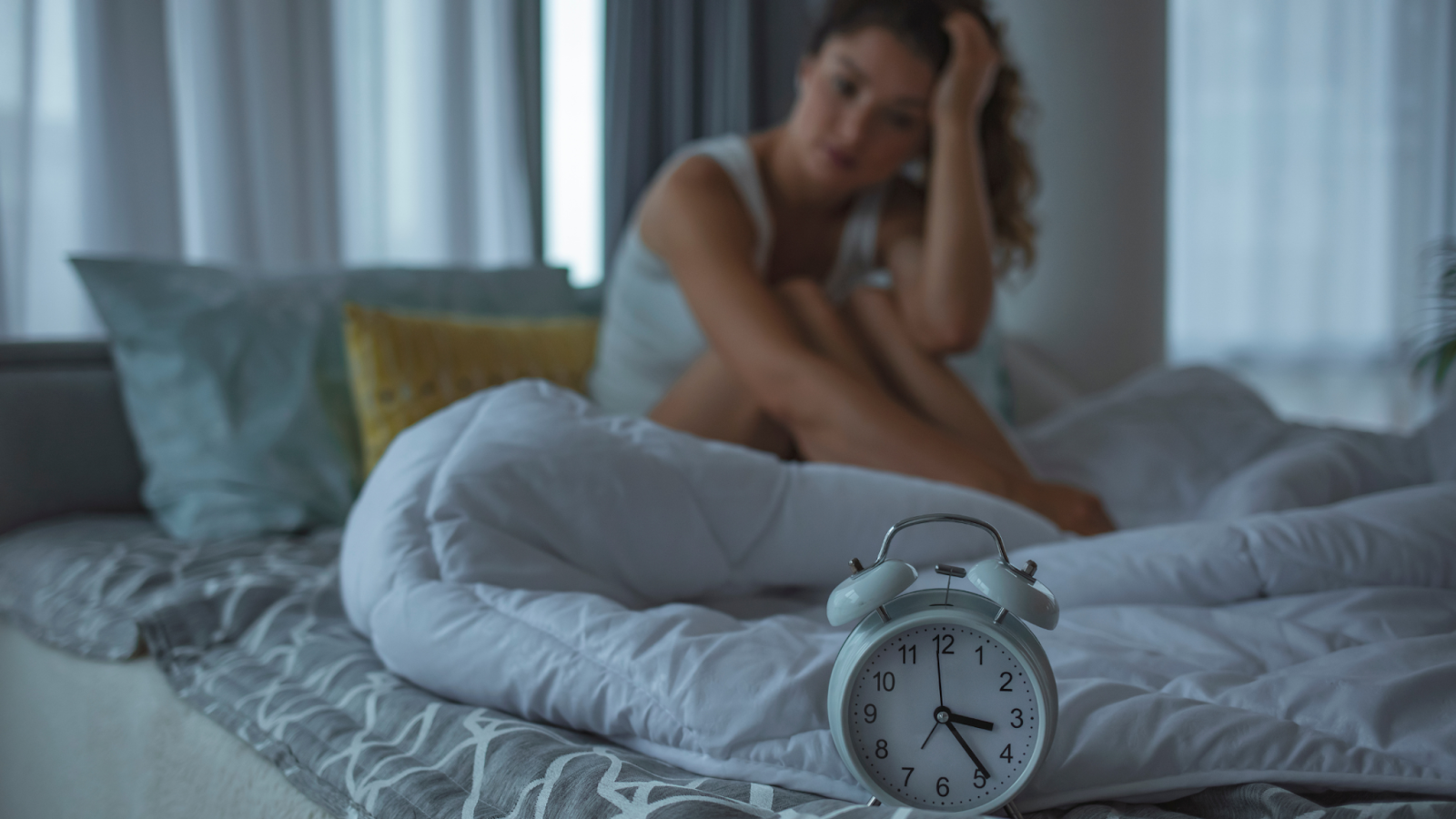 Alarm clock on bed with tired woman sitting behind