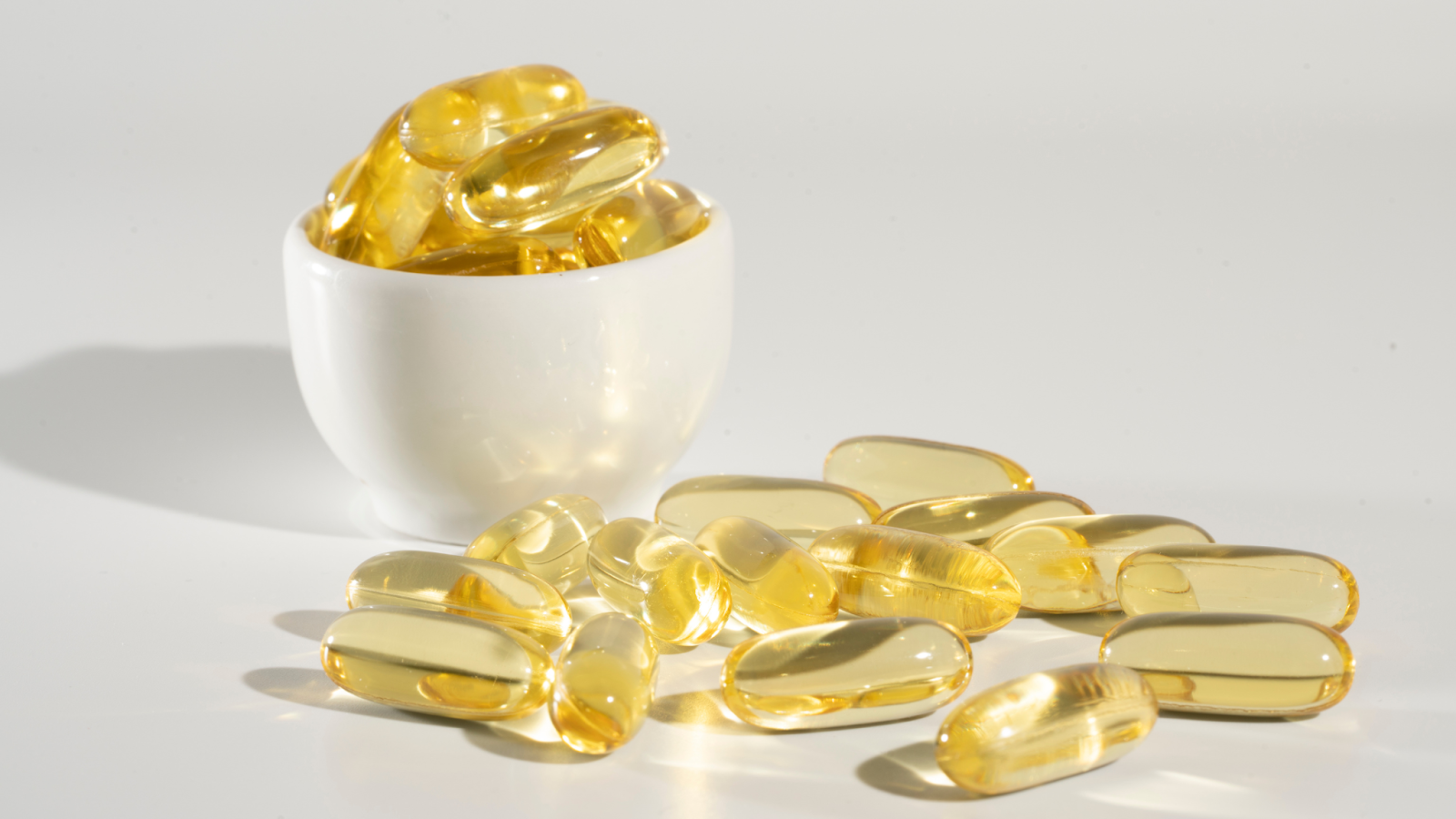 Yellow translucent vitamin capsules in white container and scattered on surface