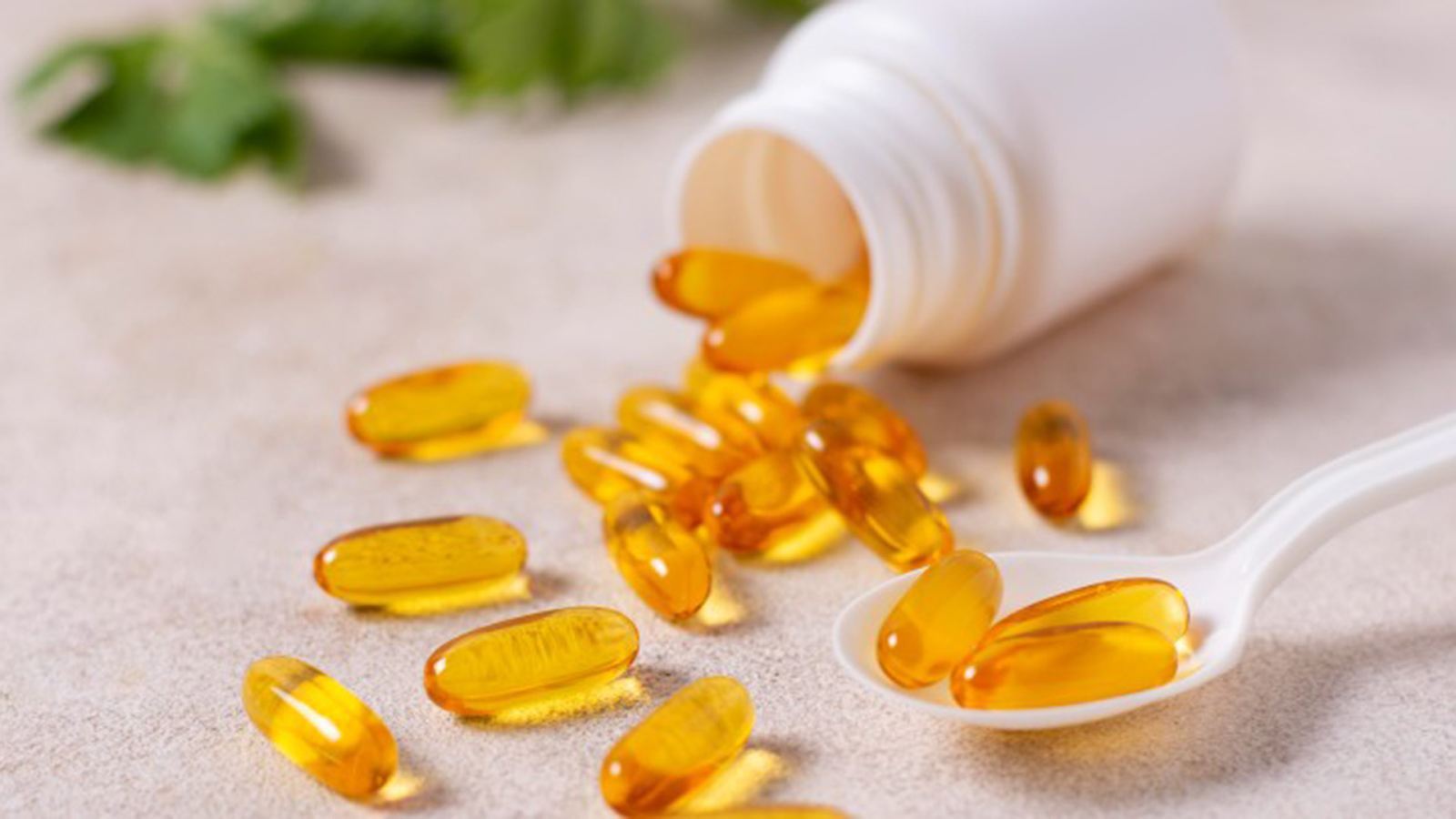 Yellow vitamin D capsules spilling from white bottle with spoon