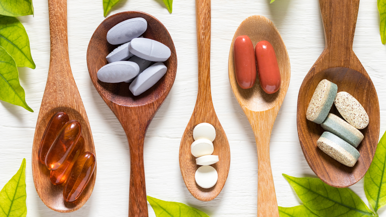 Various supplement pills and capsules on wooden spoons with green leaves