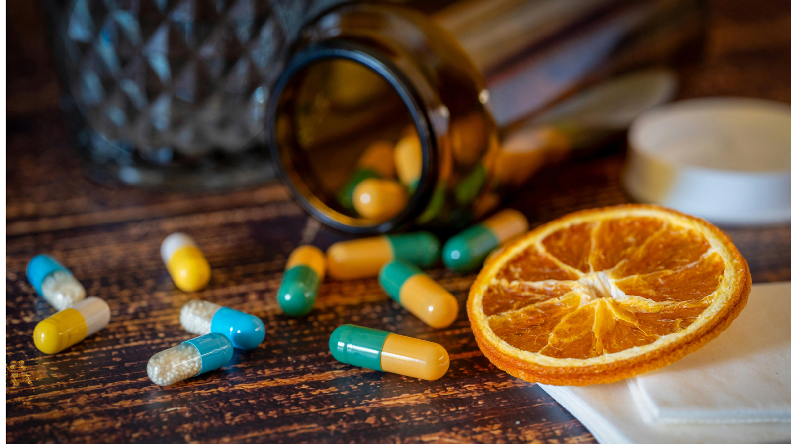 Capsule supplements spilled from bottle next to dried orange slice