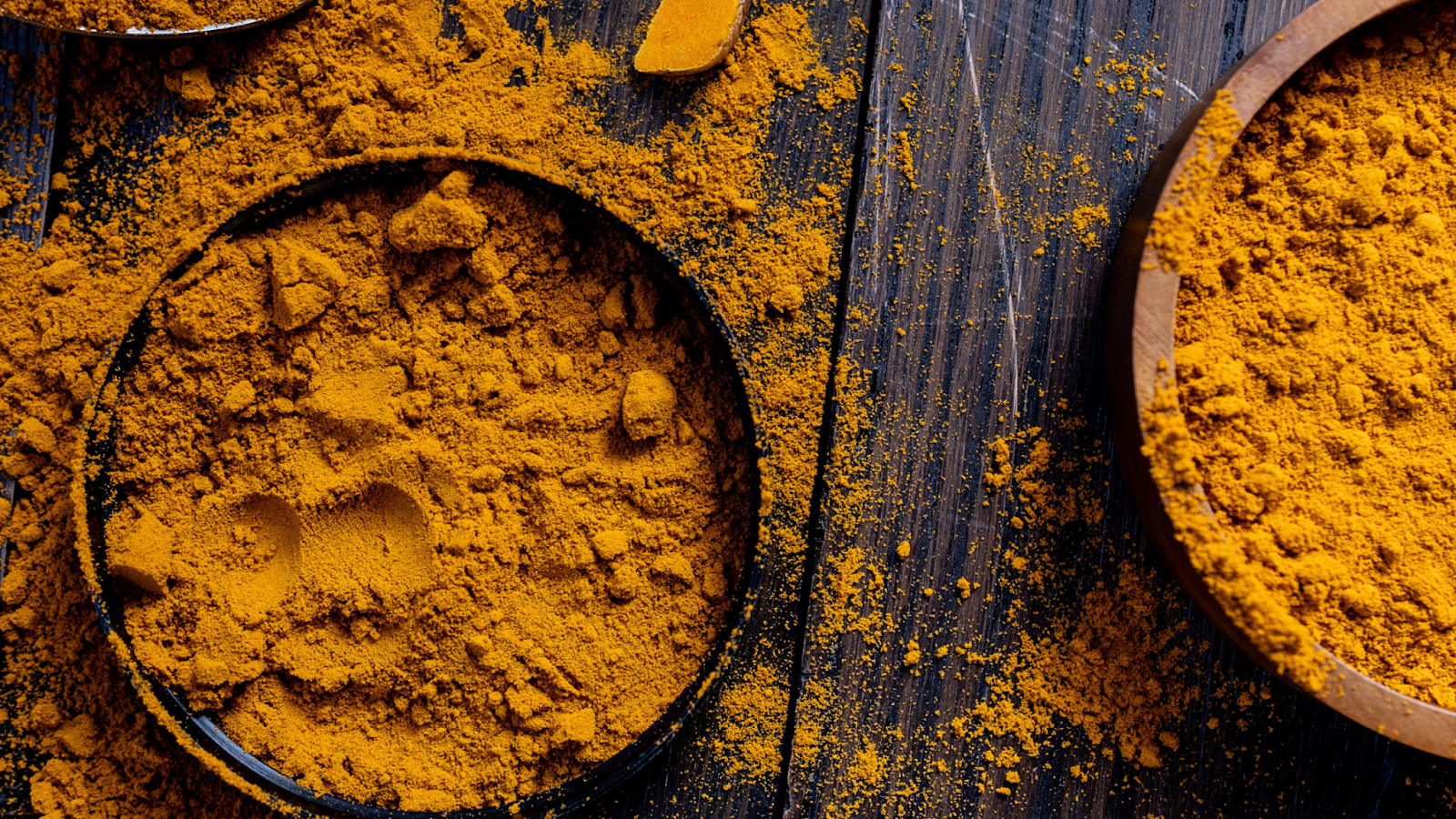 Ground turmeric powder in bowls on wooden surface