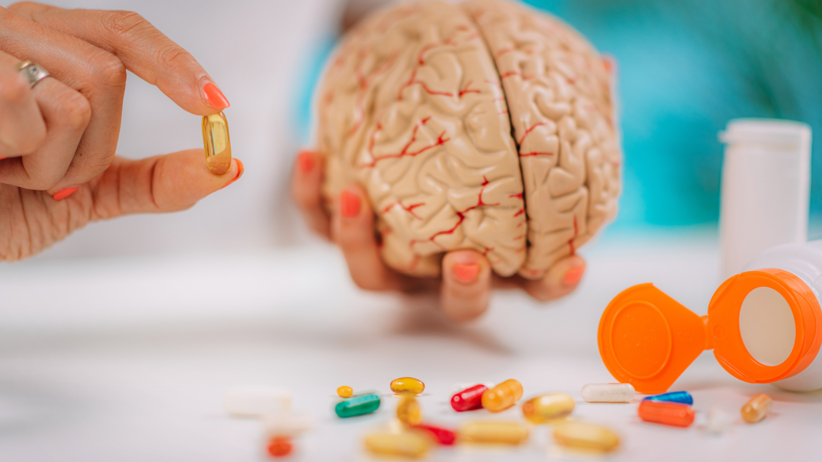 Hand holding a capsule with a brain model and scattered pills