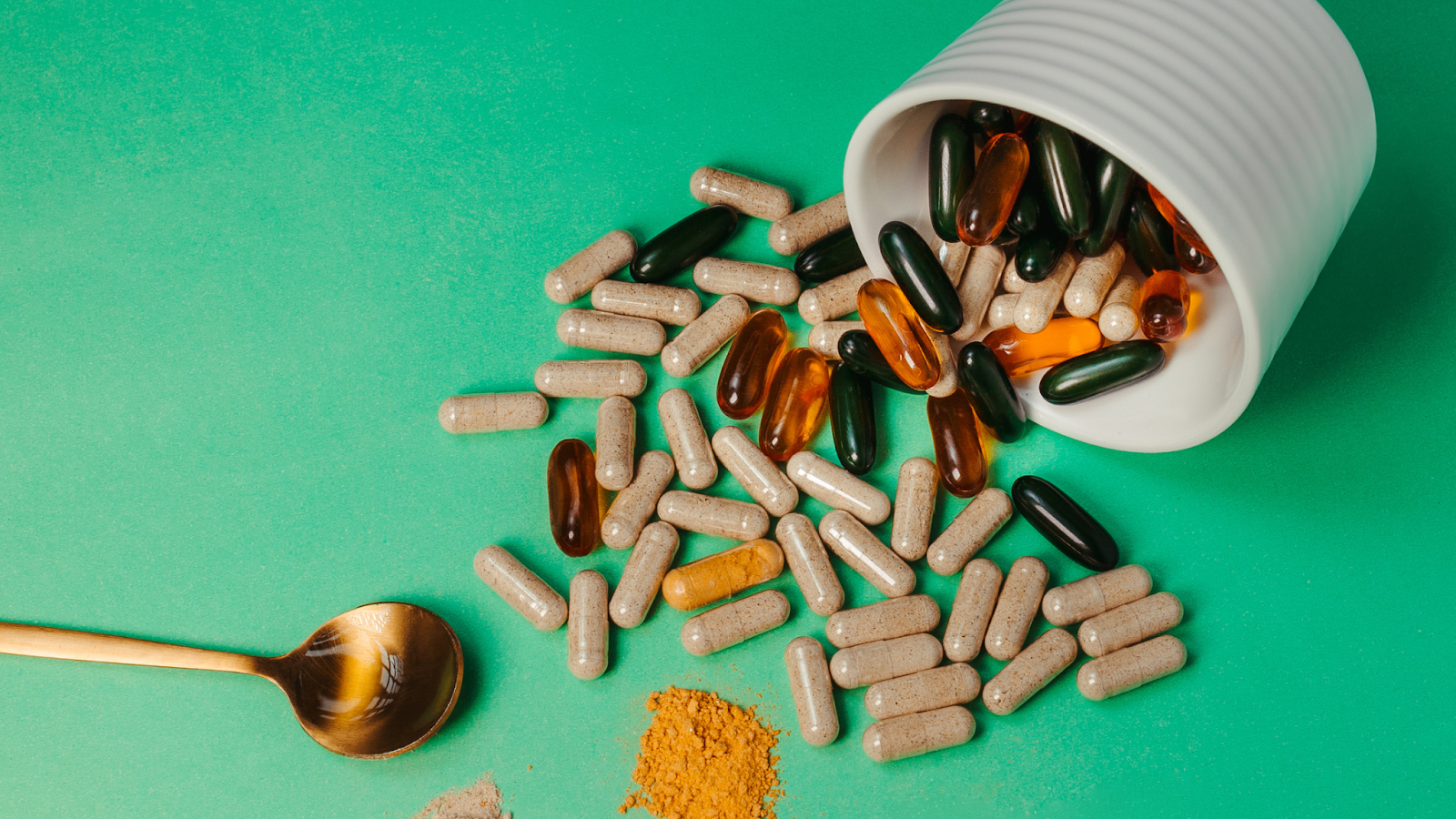 Assorted capsules and gel pills spilling from white container