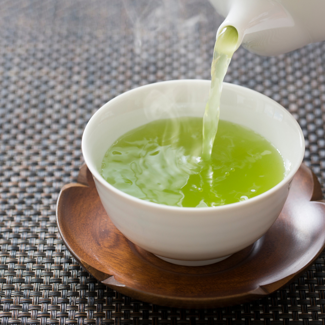 Green tea being poured into a white cup on wooden coaster