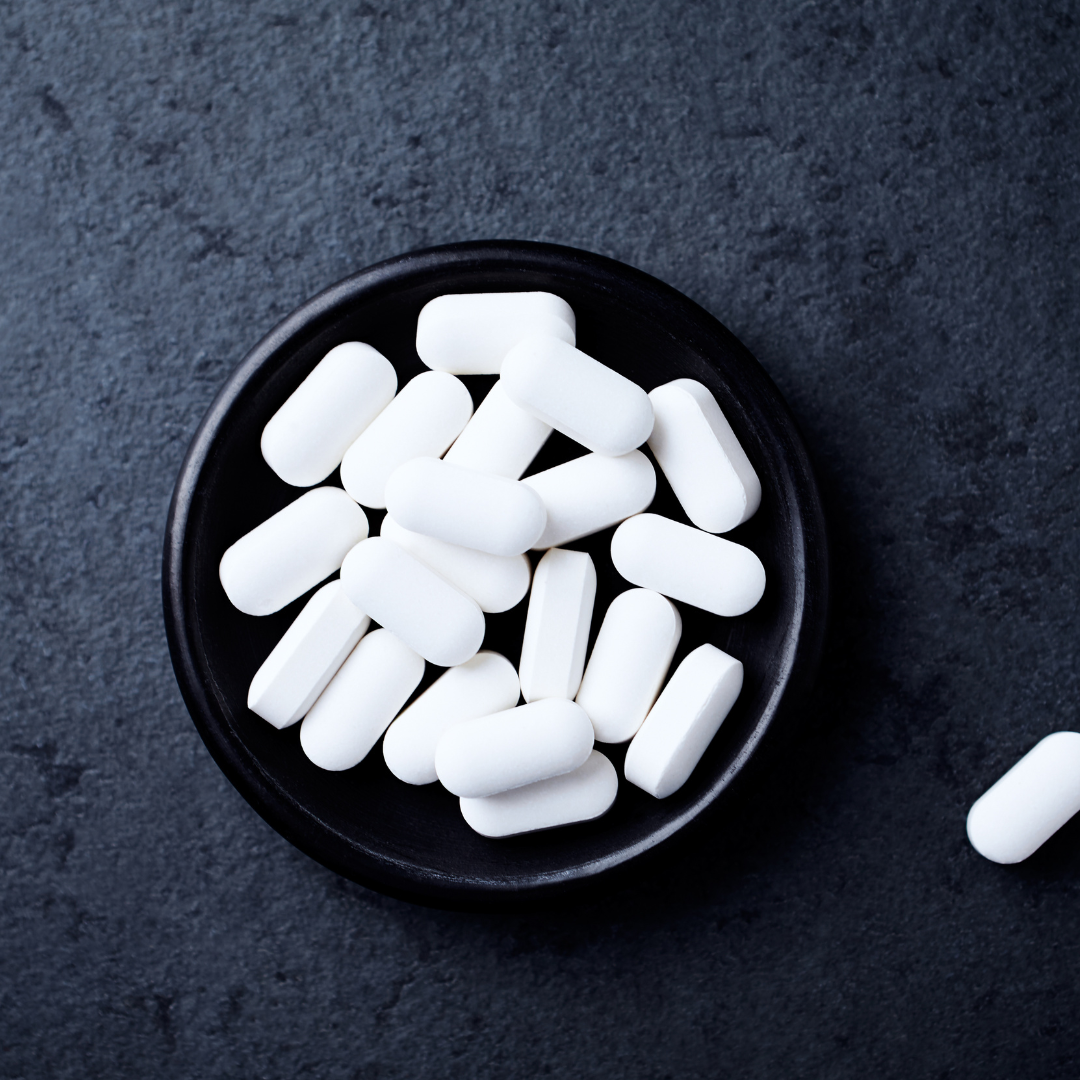 White oval pills in a black dish on dark surface