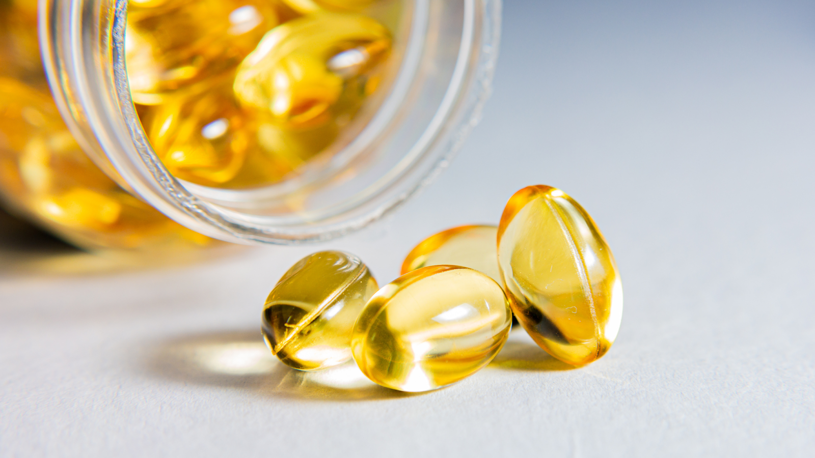 Yellow translucent softgel capsules spilling from a jar