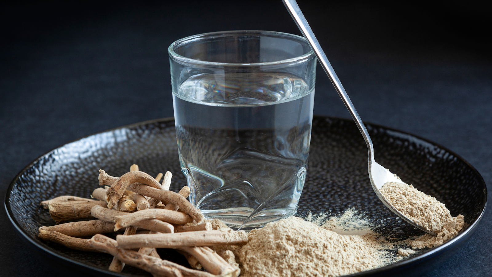 Ashwagandha roots and powdered form with glass of water on plate