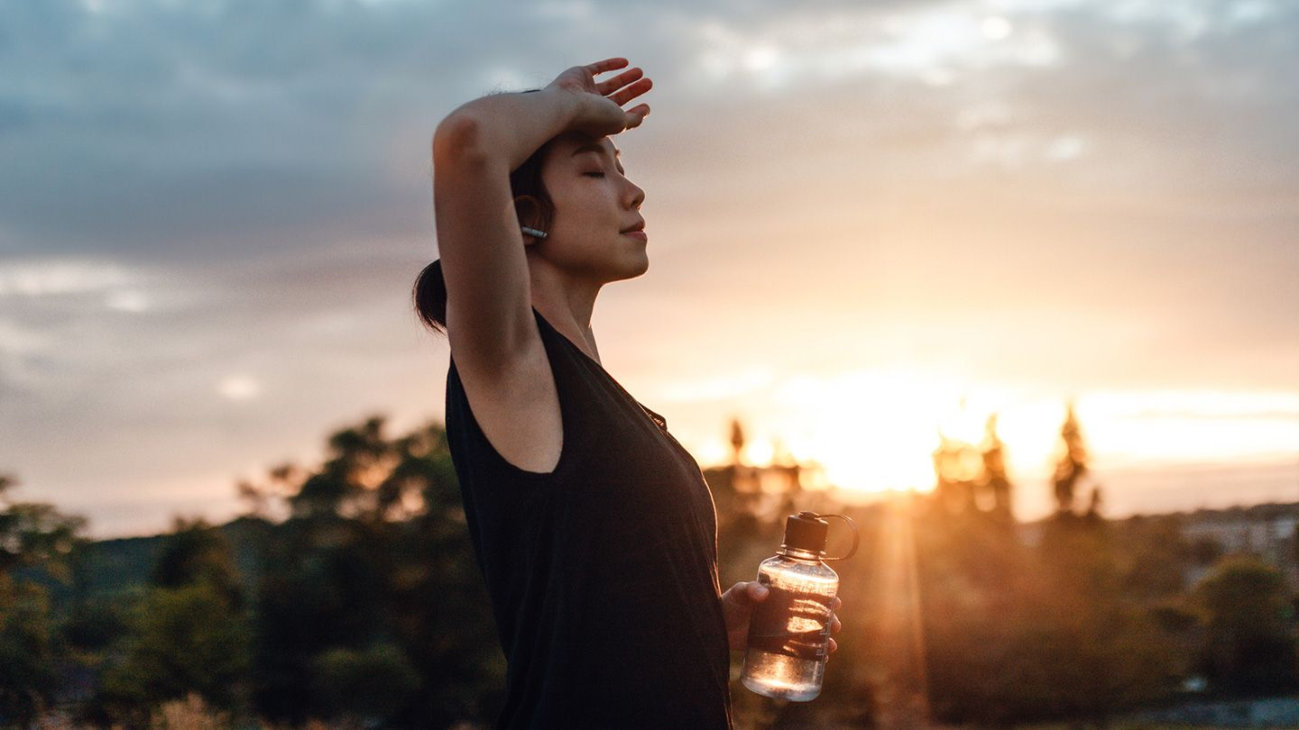 Woman holding water bottle, relaxing at sunset outdoors