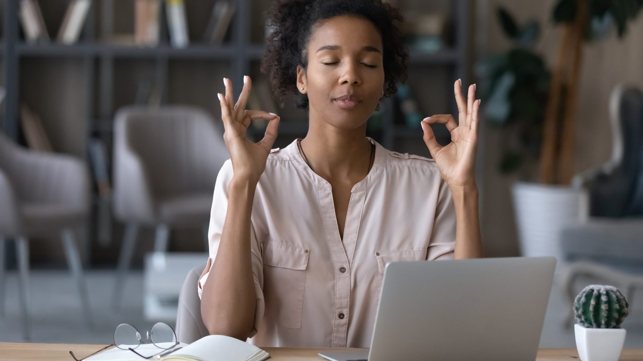 Person meditating with eyes closed at desk with laptop