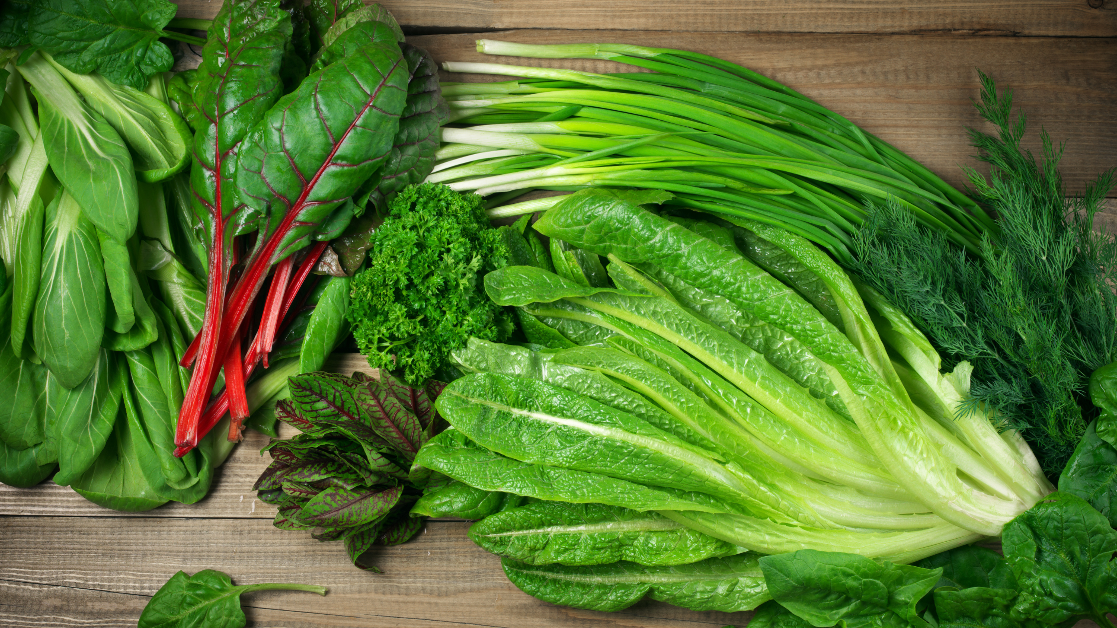 Variety of fresh leafy green vegetables on wooden surface