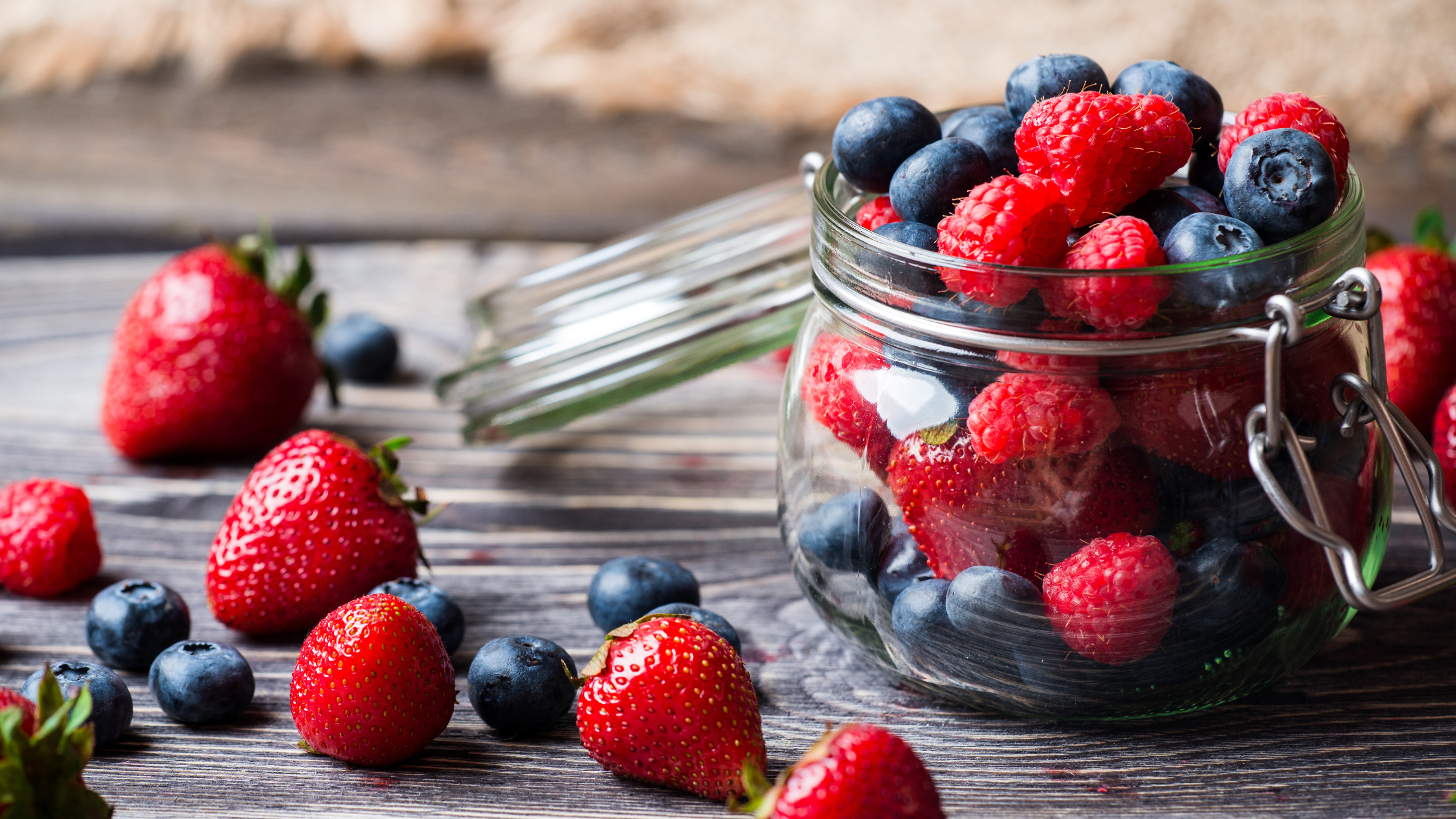 Jar filled with strawberries, blueberries, and raspberries on wooden surface