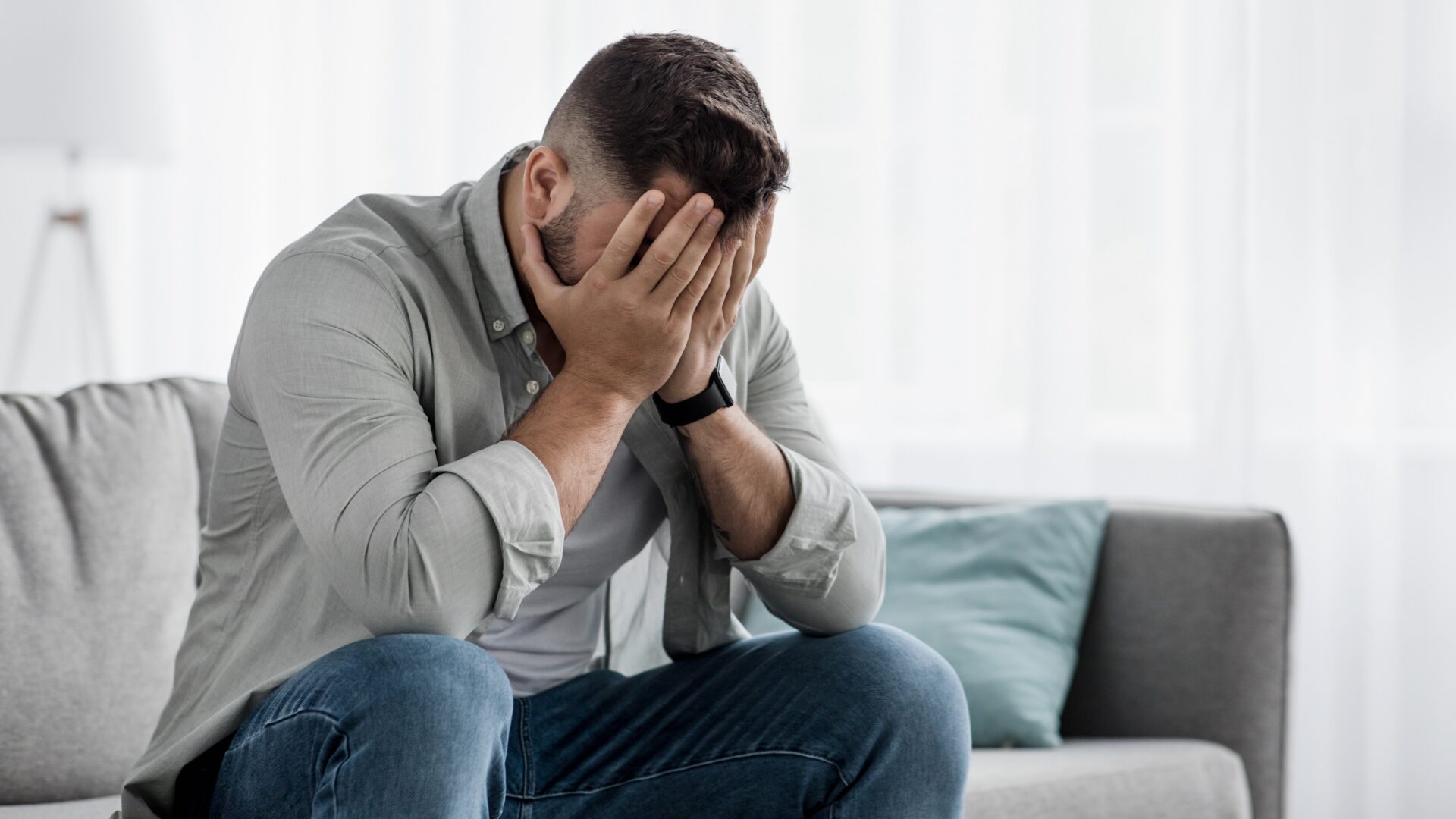 A person sits alone with their head in their hands, surrounded by shadows, visually expressing emotional distress and feelings of overwhelm.