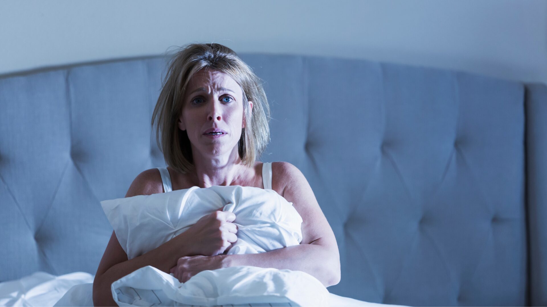 Illustration of a person experiencing a nightmare in bed, with dark, shadowy figures and anxious facial expression, symbolizing causes of nightmares.