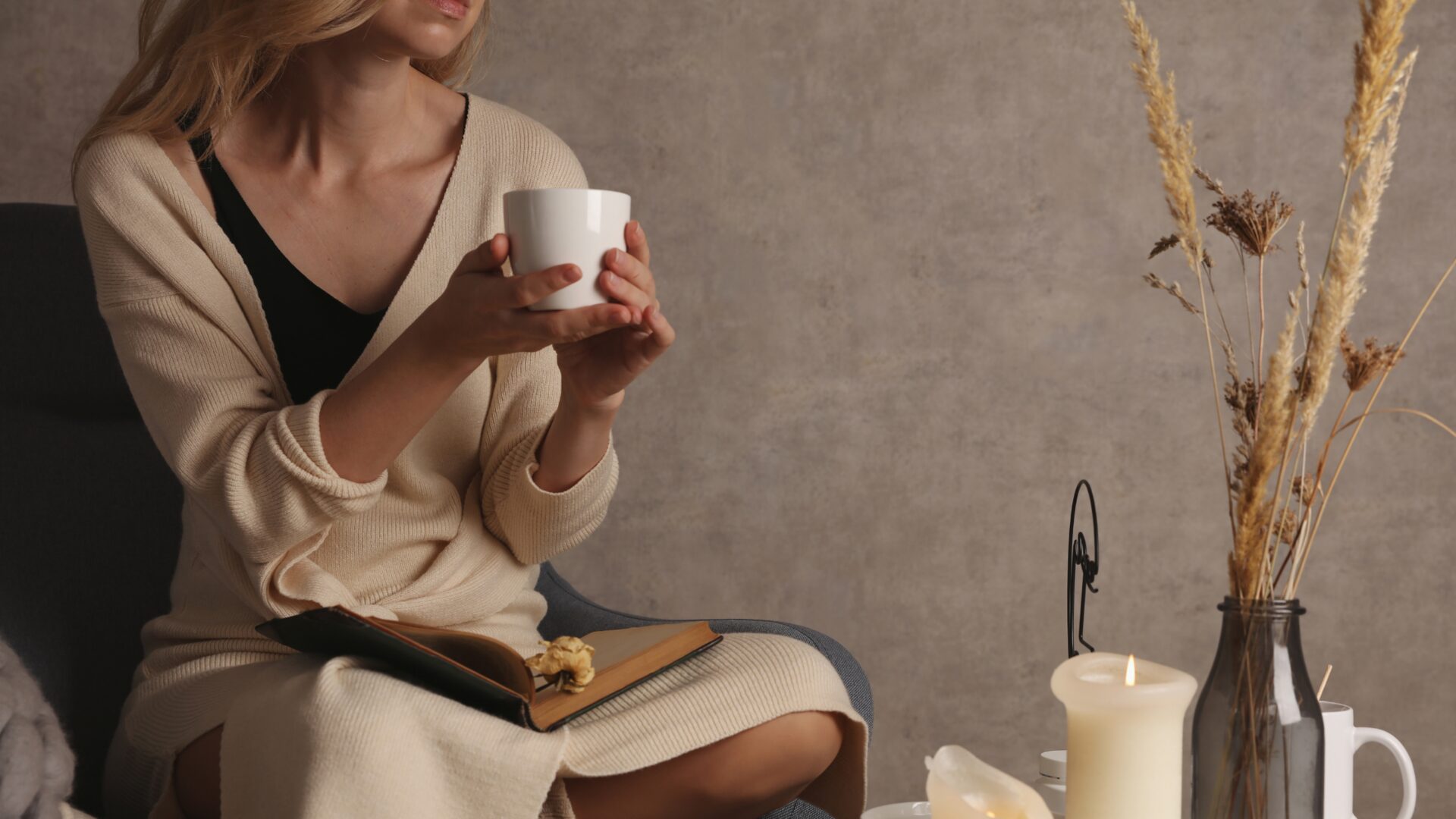 A woman practices self-care by meditating on a yoga mat, surrounded by candles, plants, and a journal in a peaceful, softly lit room.