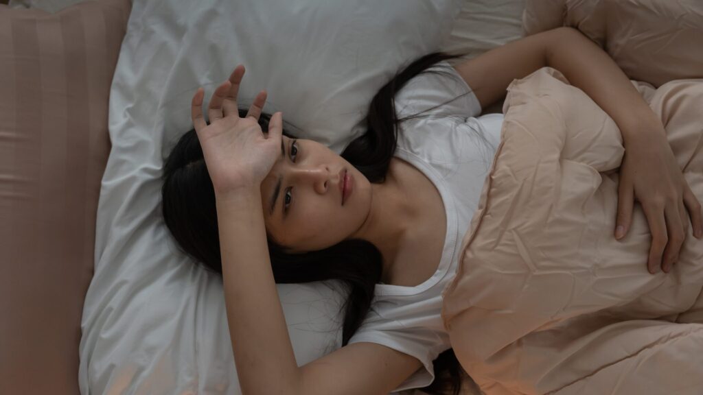 A person experiencing fragmented sleep, shown waking up multiple times during the night, appearing tired and restless in a dimly lit bedroom.