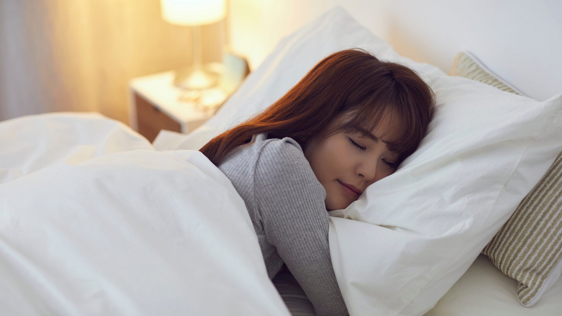 Person adjusting alarm clock and closing curtains at night, illustrating steps to fix a disrupted sleep schedule for better rest and healthier routines.