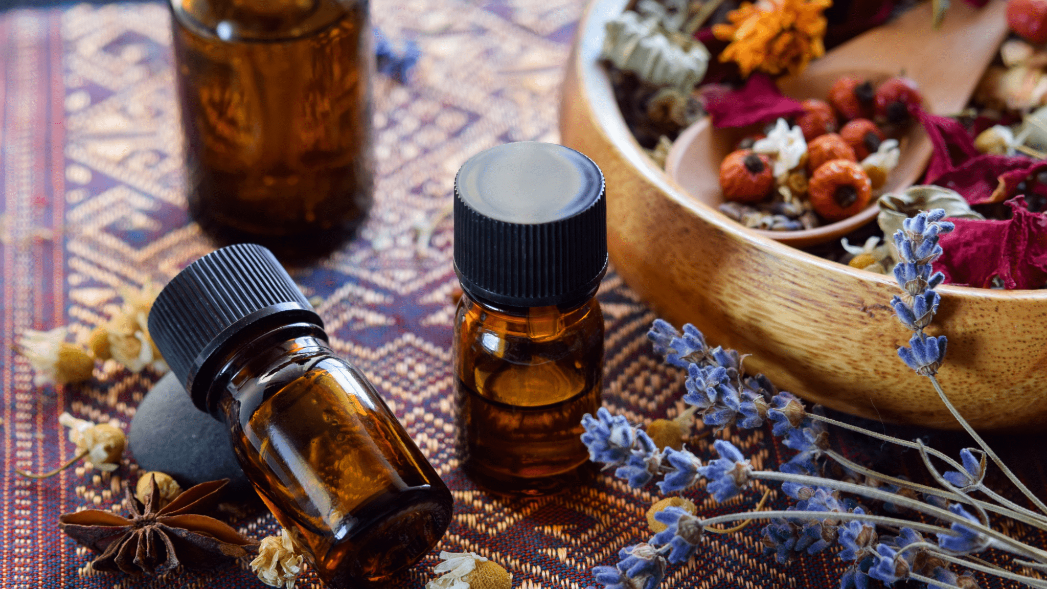 Two amber essential oil bottles with dried lavender and herbs