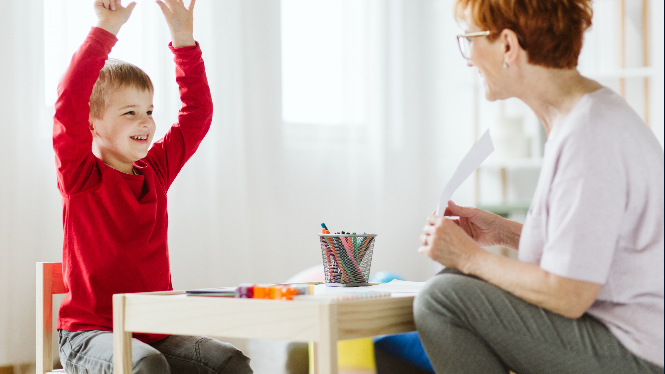 Child raising hands smiling while an adult holds paper