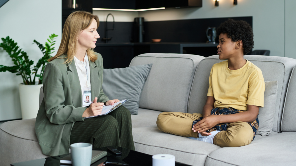 A therapist guides a young client through trauma focused cognitive behavioral therapy, using worksheets and discussion to address traumatic experiences and coping skills.