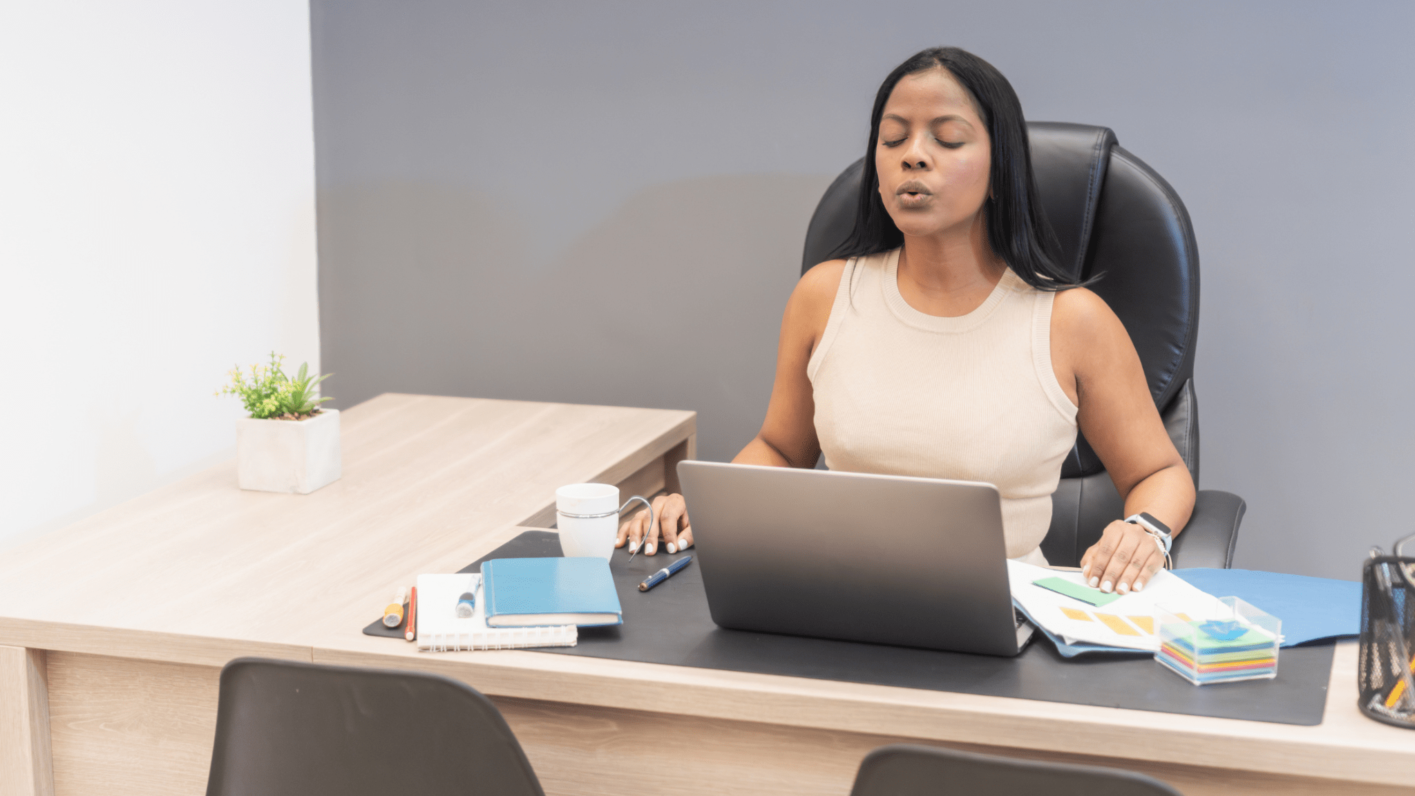 Woman sitting at desk with eyes closed and lips pursed