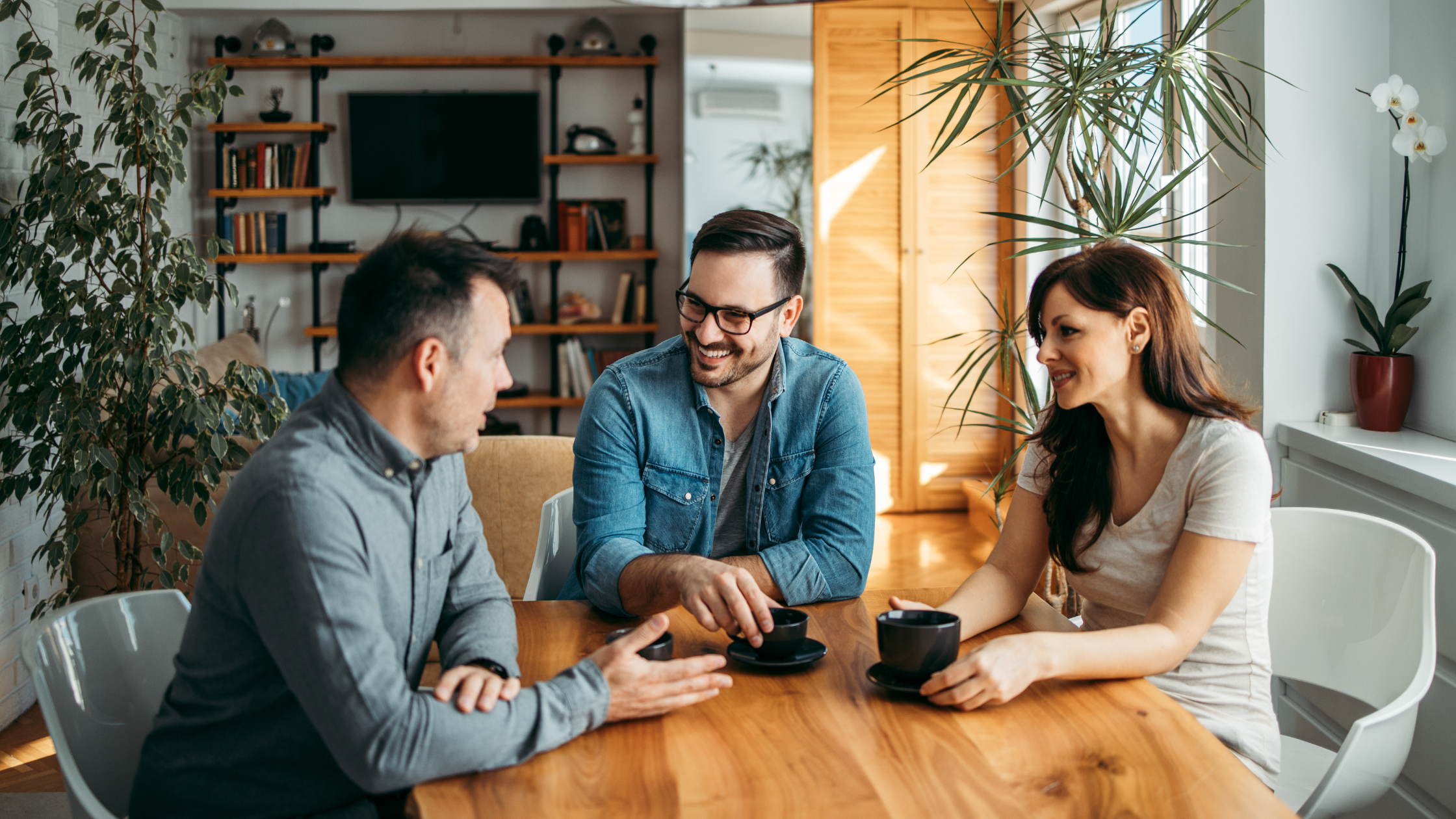 Three people smiling and talking while holding coffee cups at a table