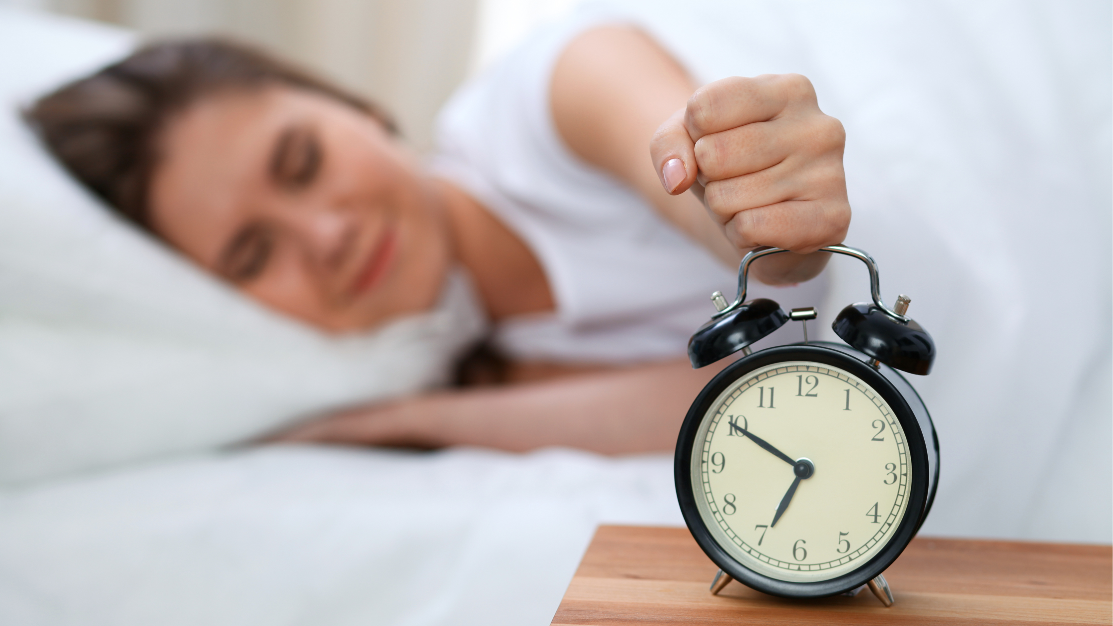 Hand reaching to turn off alarm clock near sleeping woman