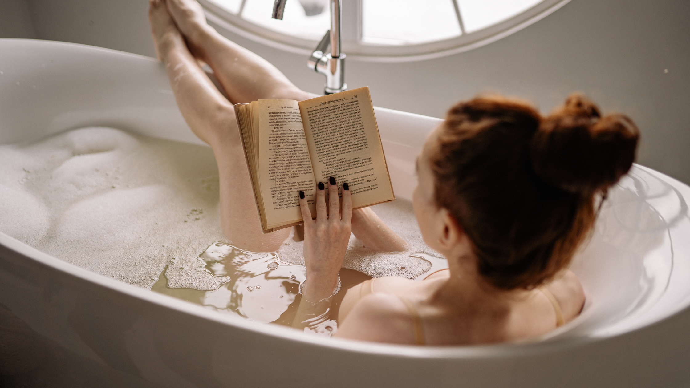 Person reading a book while relaxing in a bubble bath