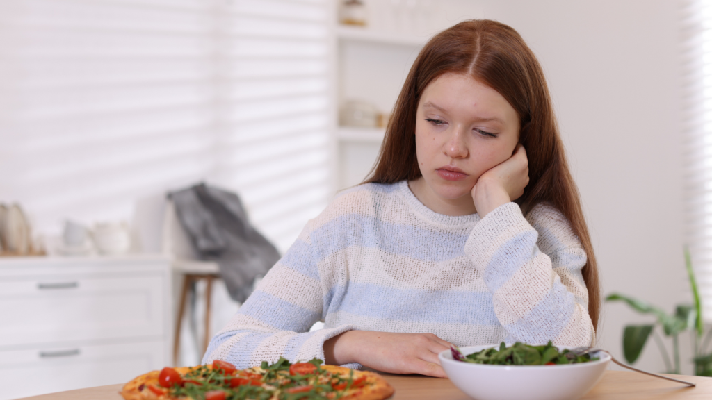 A person experiencing anxiety sits at a table with untouched food, illustrating how anxiety can cause a noticeable loss of appetite.